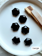 Overhead view of multiple large faceted Black Obsidian hexagon crystals in a white dish, polished sacred geometry carvings for grounding and protection