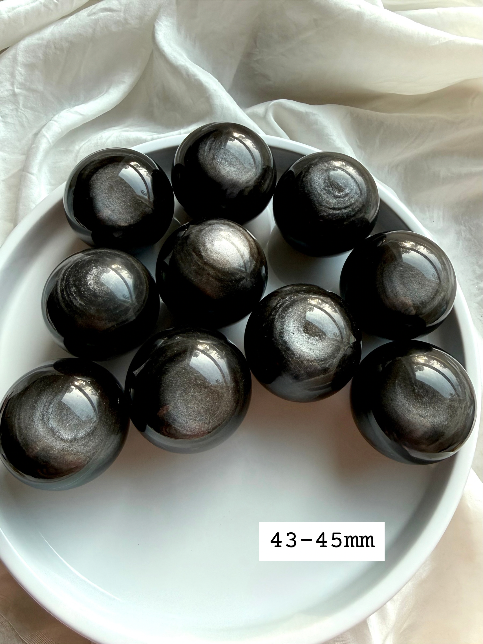Silver Sheen Obsidian crystal spheres size 43-45mm on white tray, polished obsidian balls with luminous silver flash for protection and spiritual grounding