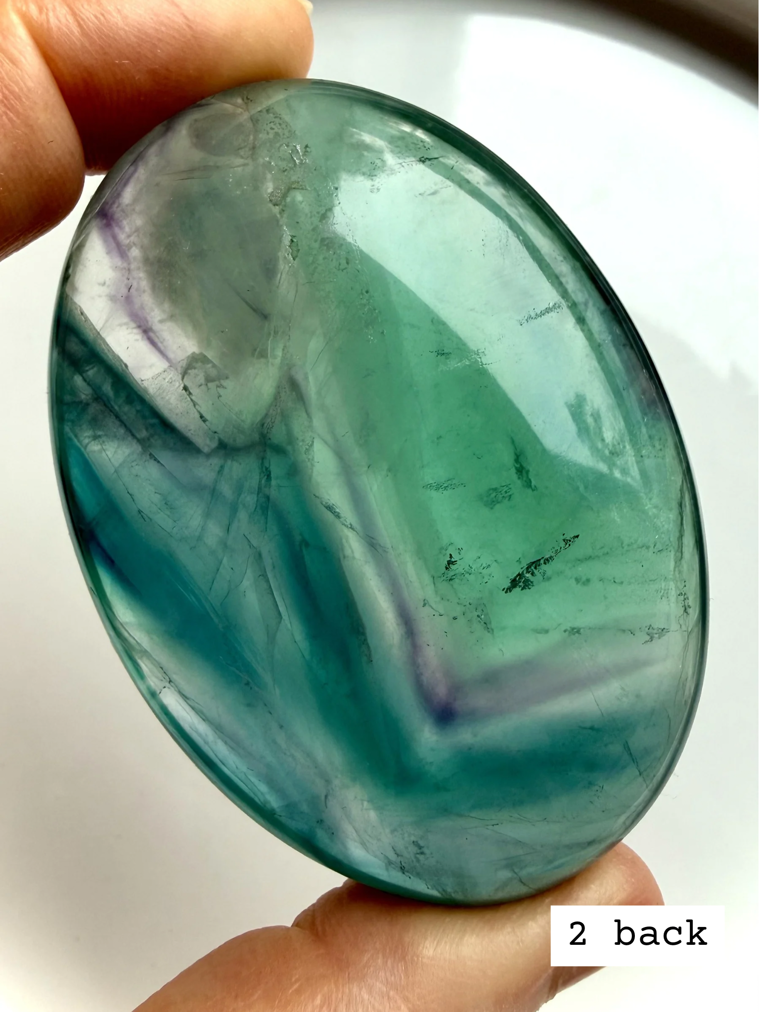Teal fluorite palm stone #2 back view displaying saturated blue green bands and translucent depth
