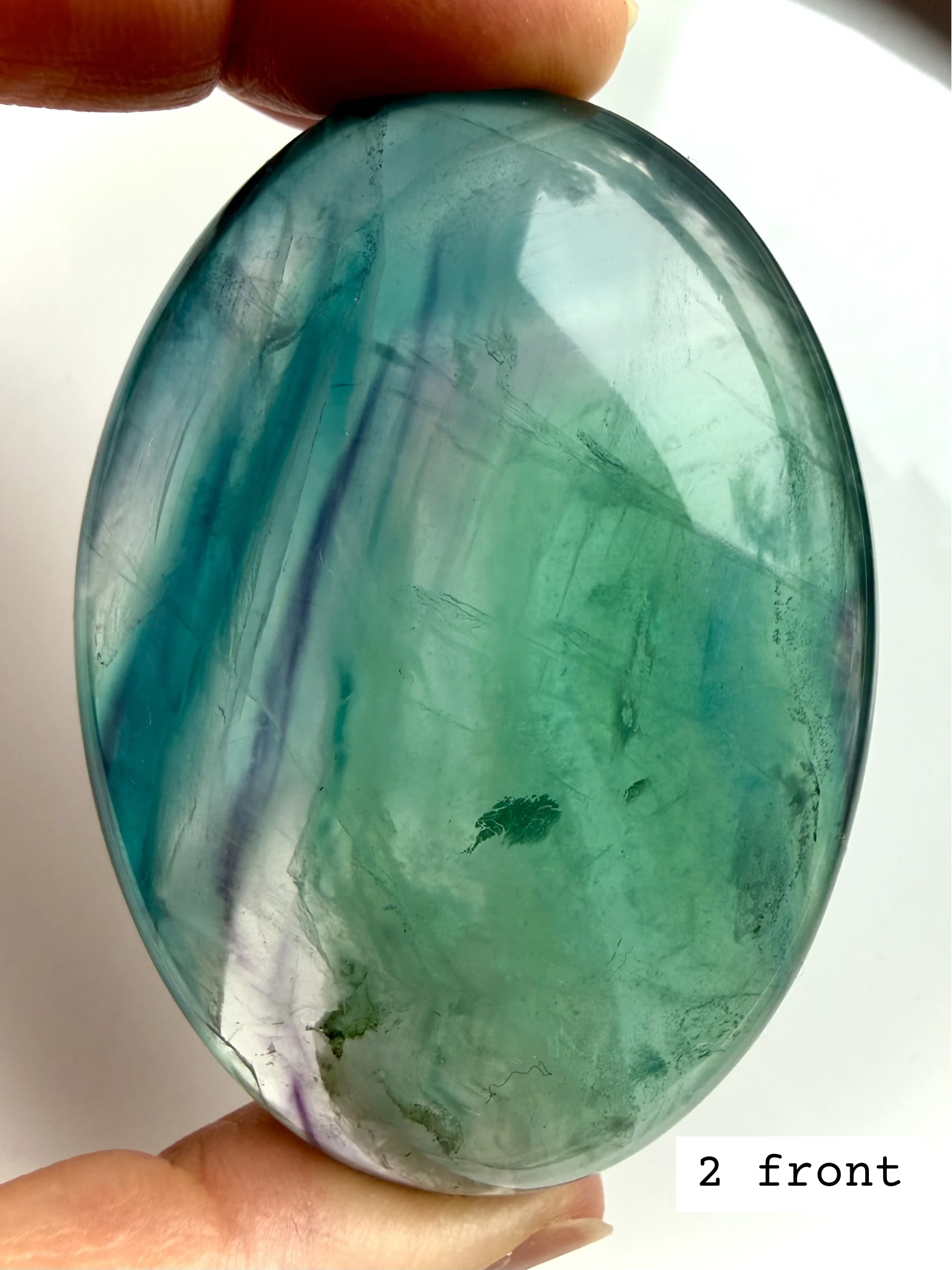 Teal fluorite palm stone #2 front view held to the light with bold blue green marbling and polished surface