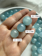 Mini Aquamarine crystal spheres with size labels held in hand – calming blue March birthstone stone