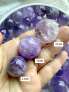 smoky amethyst mini spheres in hand showing size comparison of 22mm, 28mm, and 31mm small crystal balls with natural inclusions