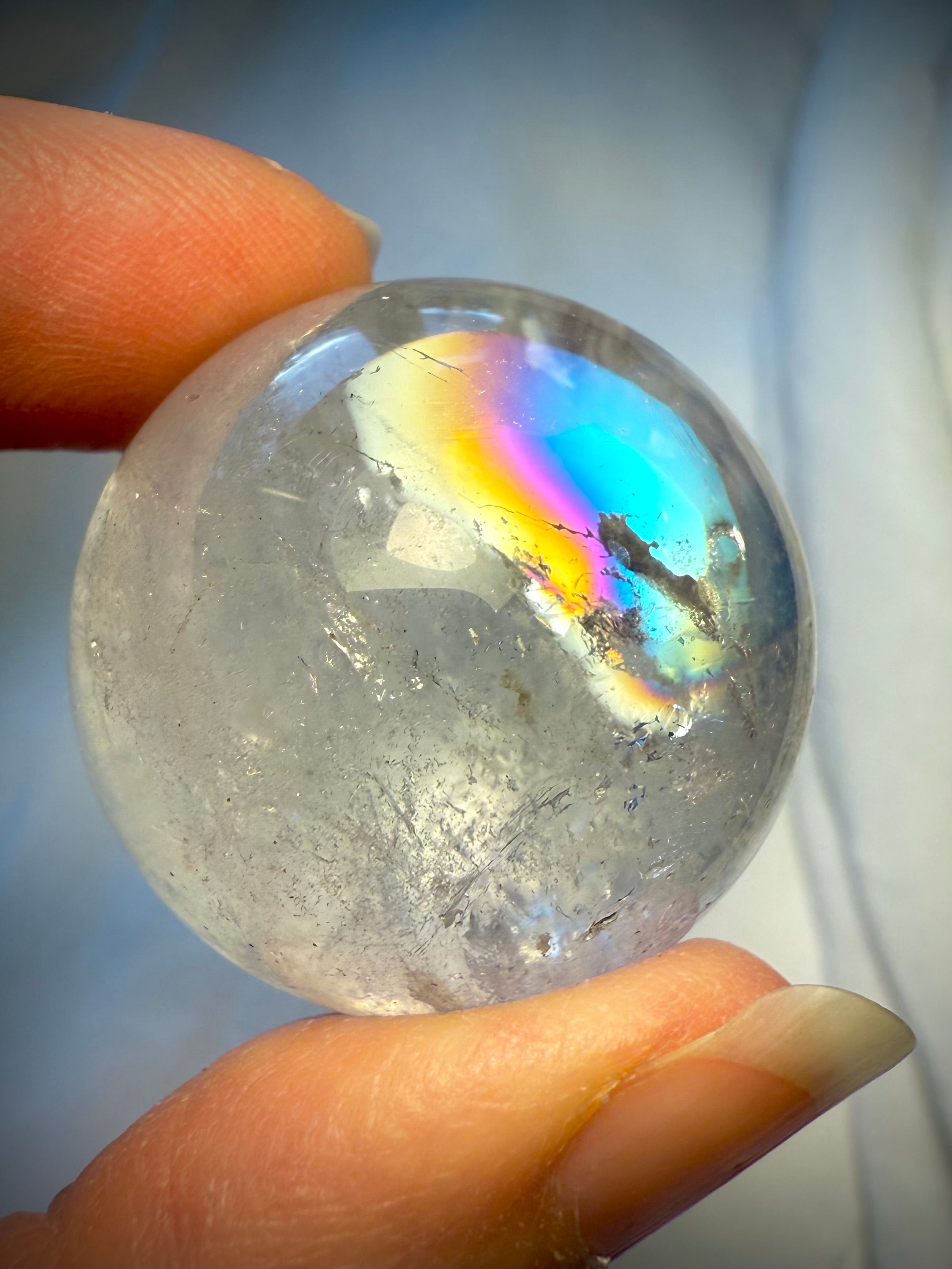 Stunning Rainbow Quartz sphere with intense prismatic flash held at fingertips – high-vibration crystal for crown chakra and lightwork