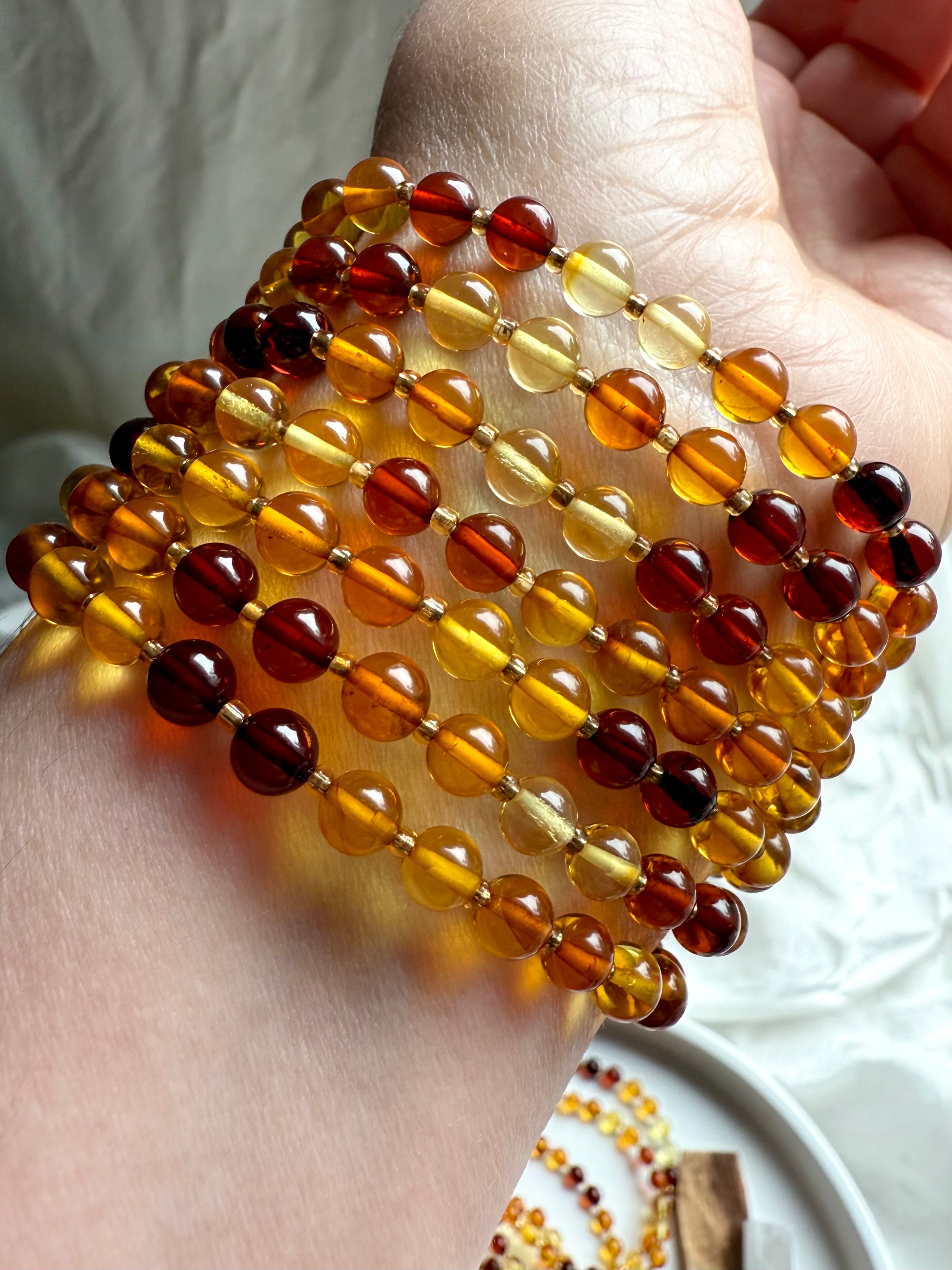 Close-up of polished Baltic amber bead bracelets in warm golden, honey, and cognac tones – Solar Plexus crystal jewelry for energy, confidence + vitality