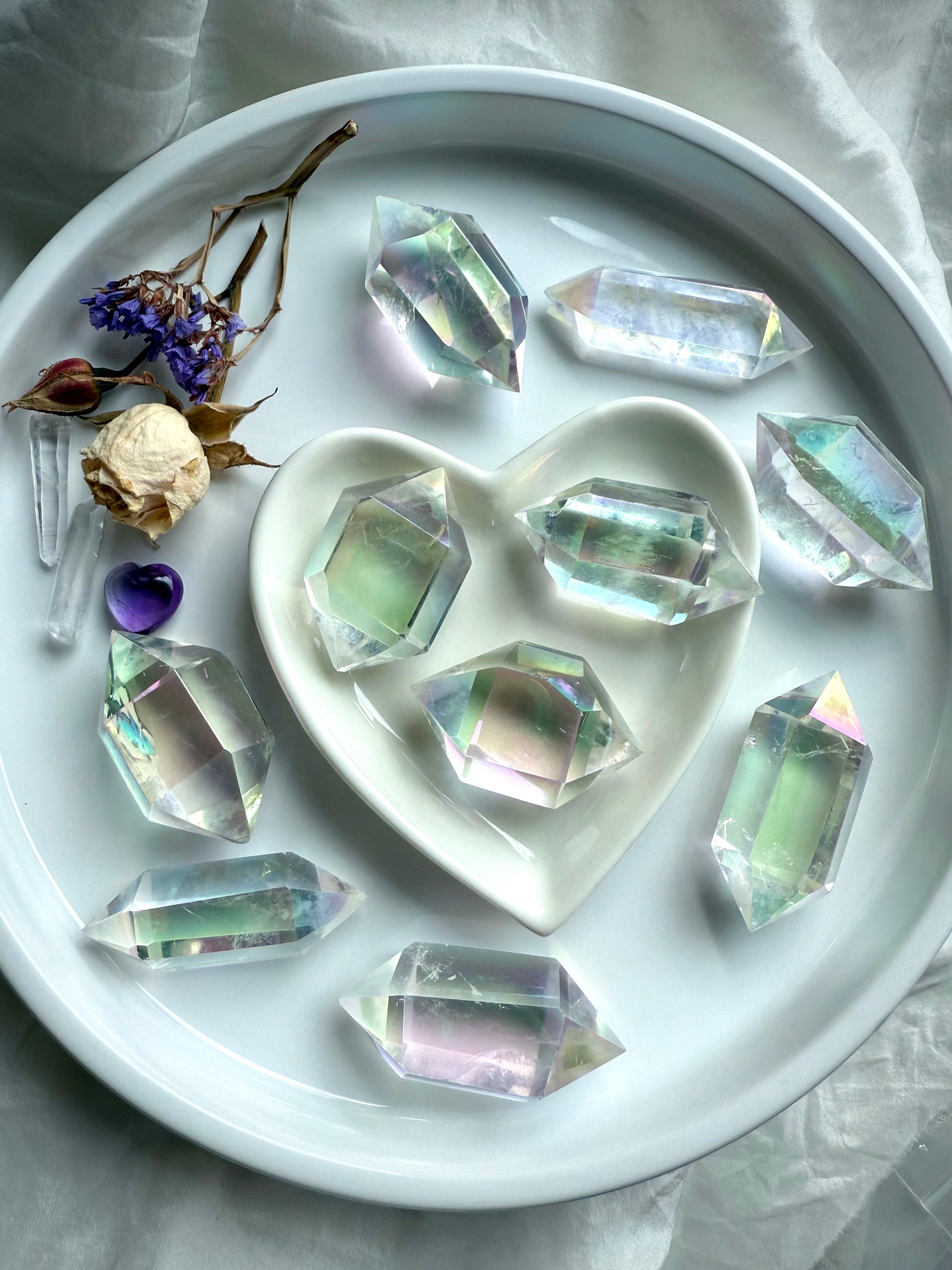 Iridescent Angel Aura Quartz double terminated crystal points in a round dish with heart-shaped bowl, rainbow sheen reflecting light
