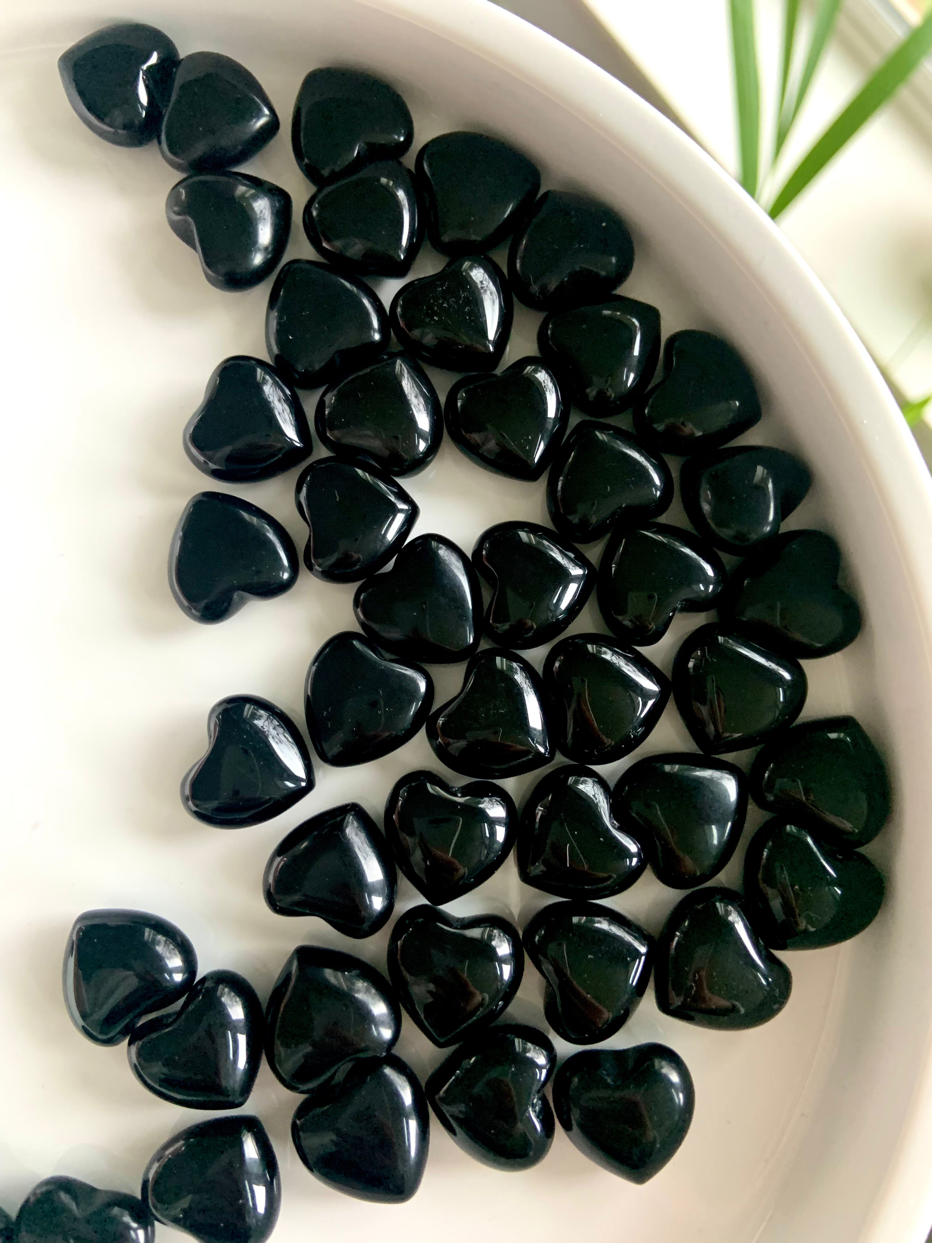 Glossy mini Black Obsidian hearts filling a white ceramic bowl — crystal carvings for grounding, protection, and sacred space rituals