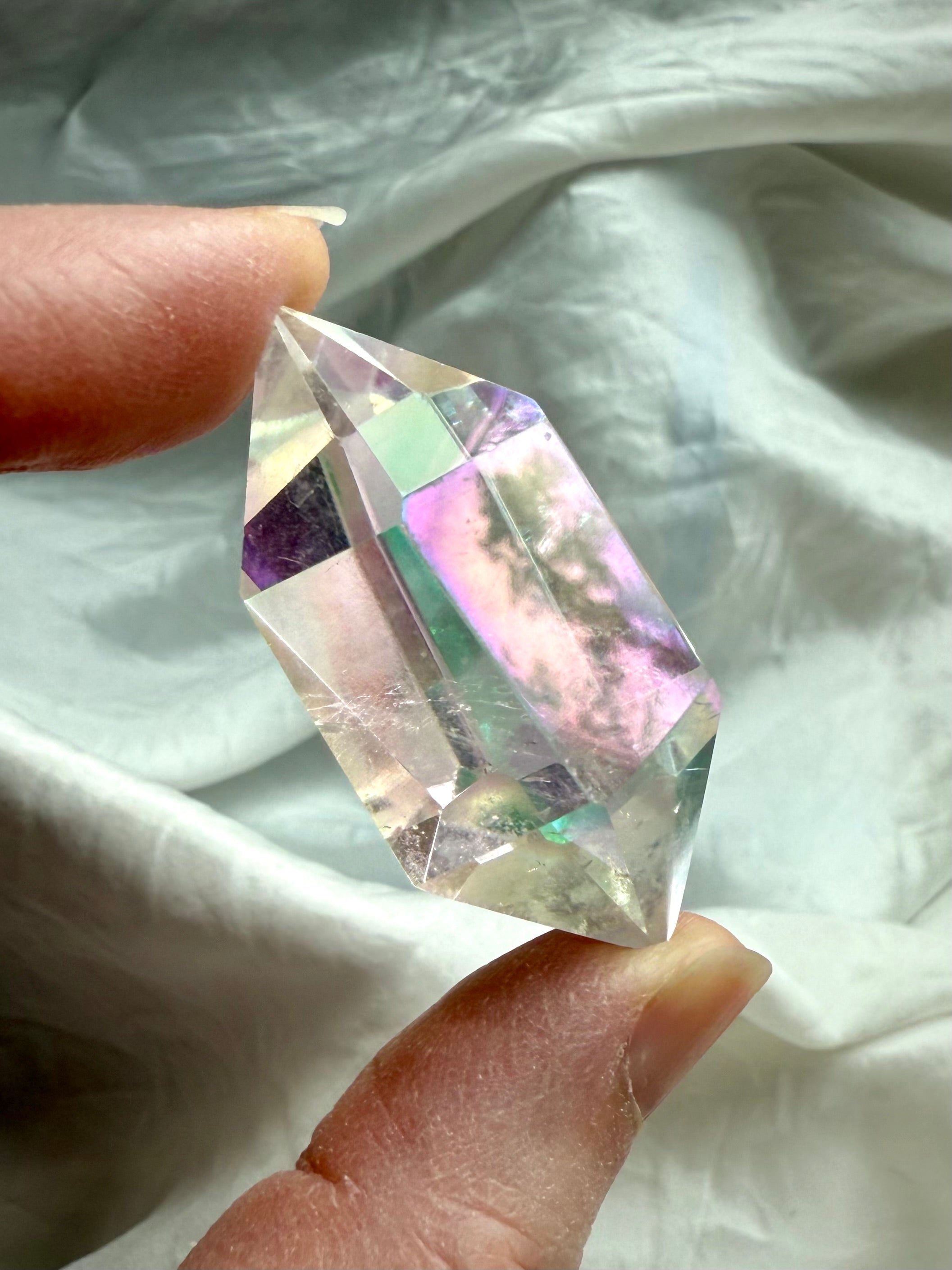 Closeup of clear Angel Aura Quartz DT crystal held in hand showing sharp double terminations and luminous rainbow aura coating