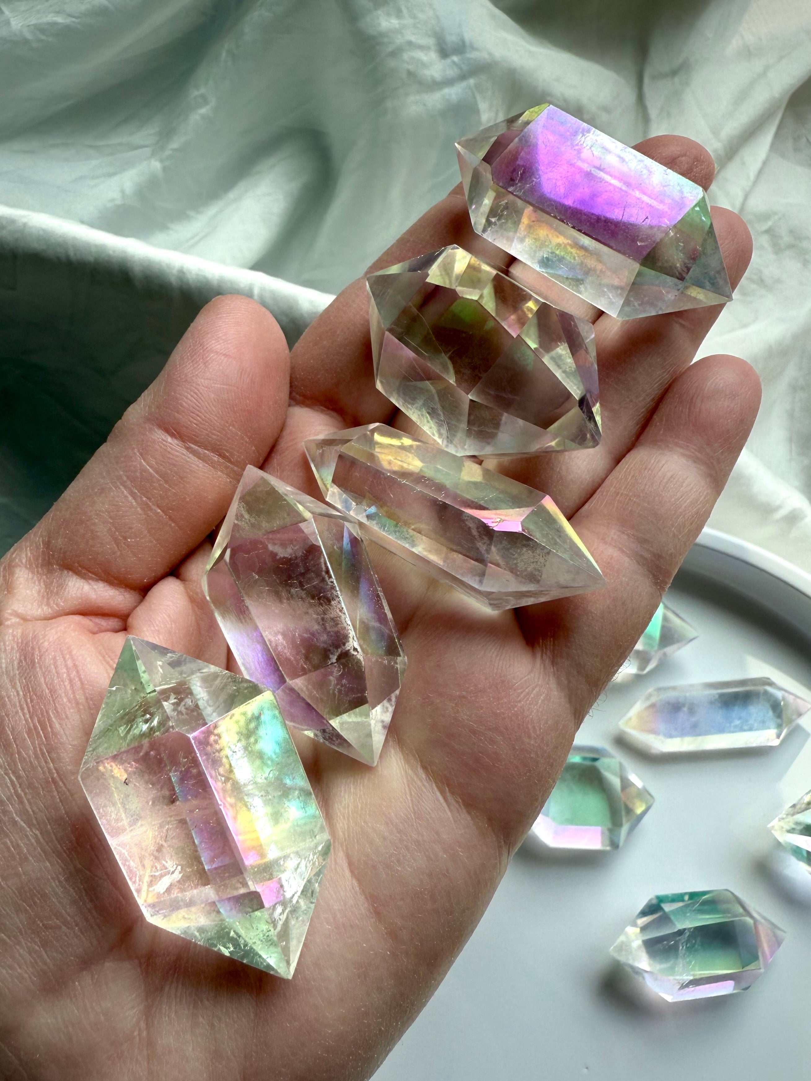 Hand holding several Angel Aura Quartz double terminated crystal points with rainbow sheen and faceted clarity