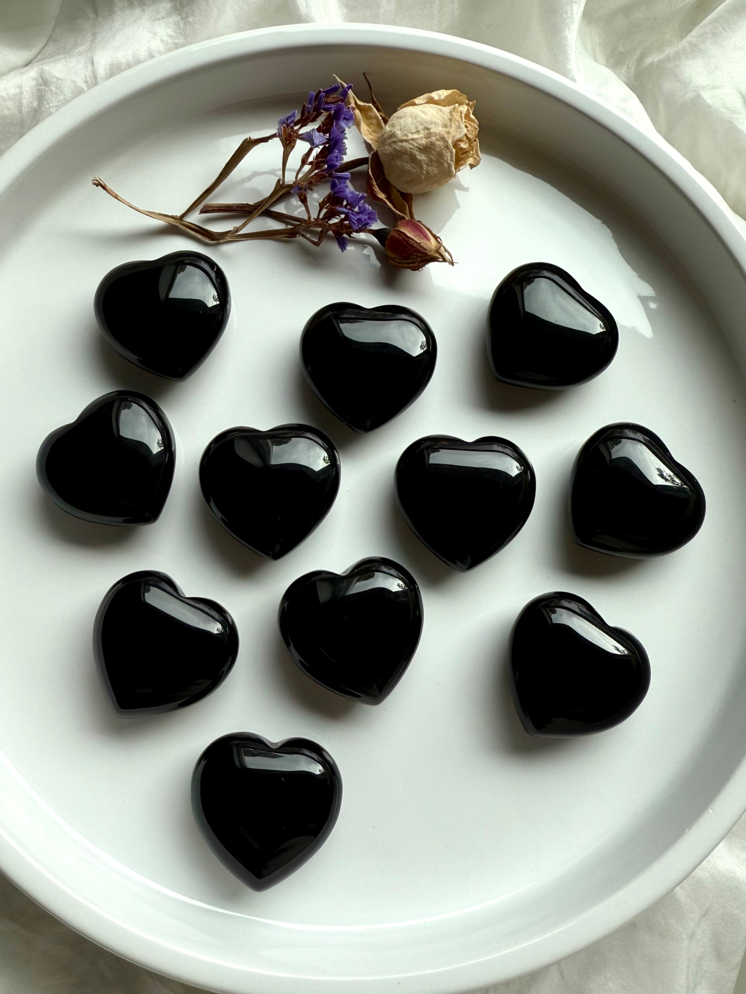 Group of Black Obsidian hearts in a white dish with flowers — protective crystals for altar décor, energy clearing, and shadow work.