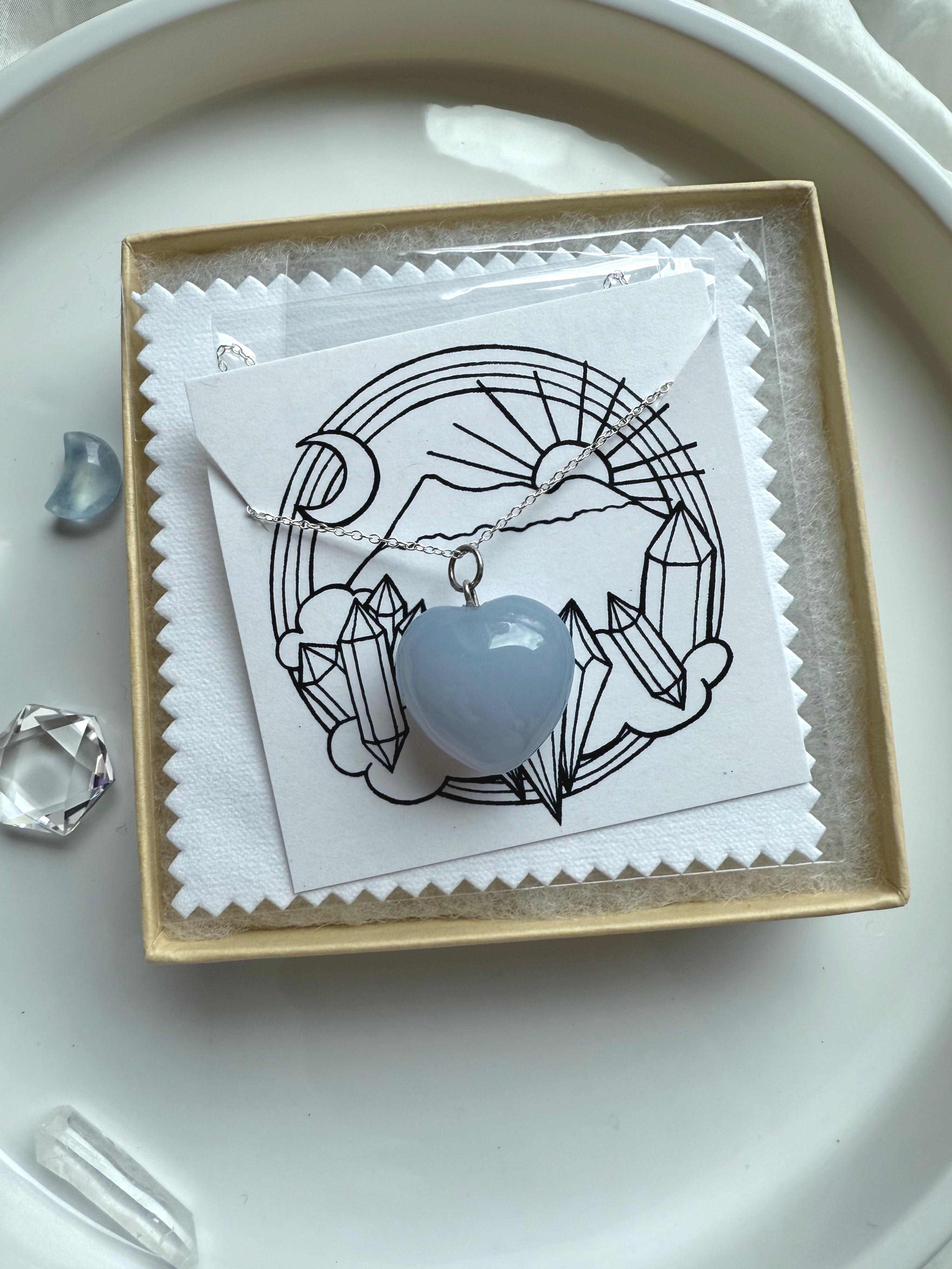 Blue Chalcedony heart necklace on silver chain, packaged with crystal-themed insert card and white polishing cloth.