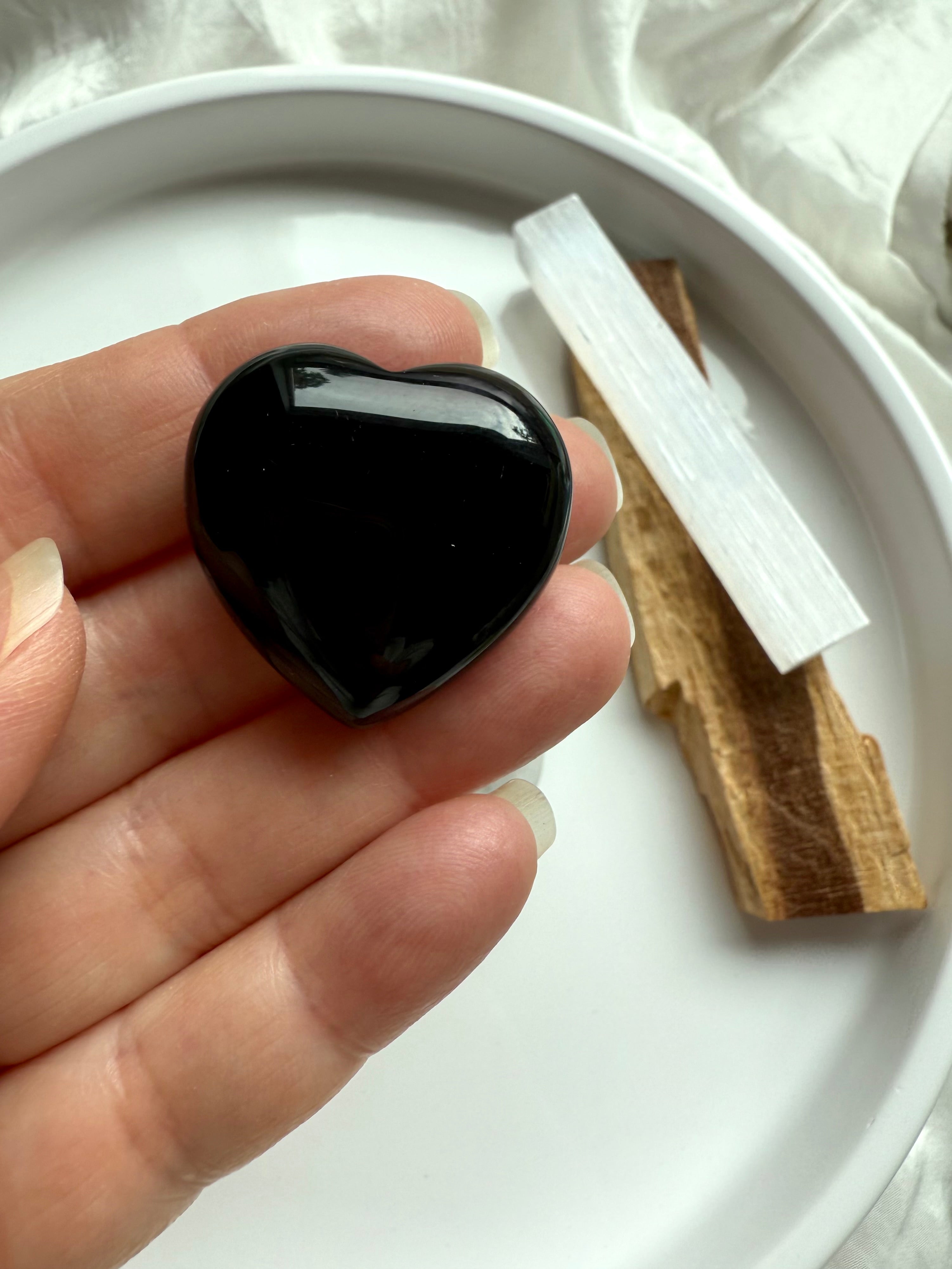 Hand holding a glossy Black Obsidian heart — grounding crystal for aura protection, meditation, and emotional release.