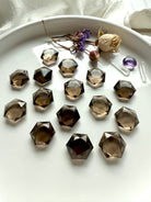 Collection of smoky quartz hexagons in a white tray with roses, amethyst heart, and quartz points – Root Chakra crystals for ritual and energy work.