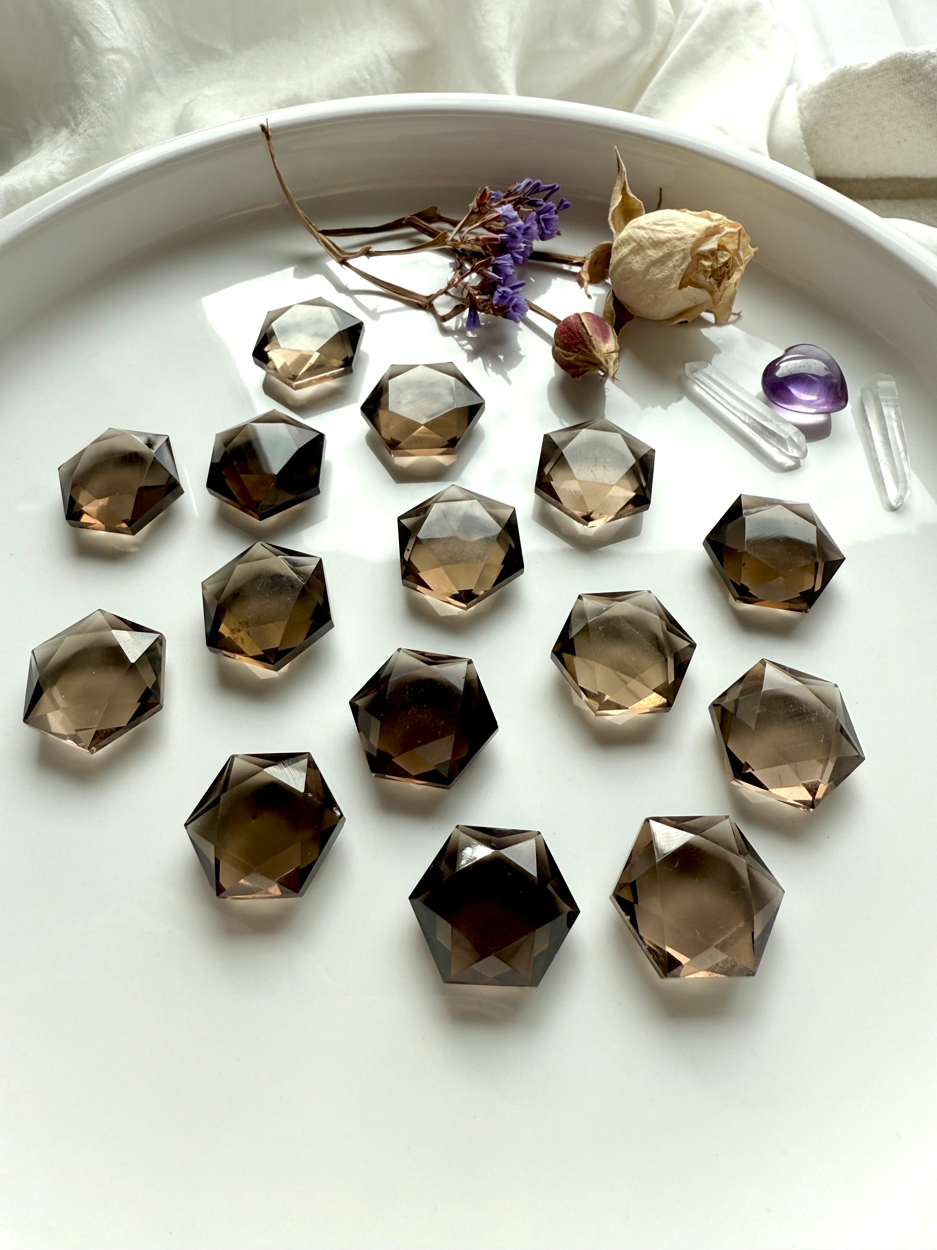 Collection of smoky quartz hexagons in a white tray with roses, amethyst heart, and quartz points – Root Chakra crystals for ritual and energy work.