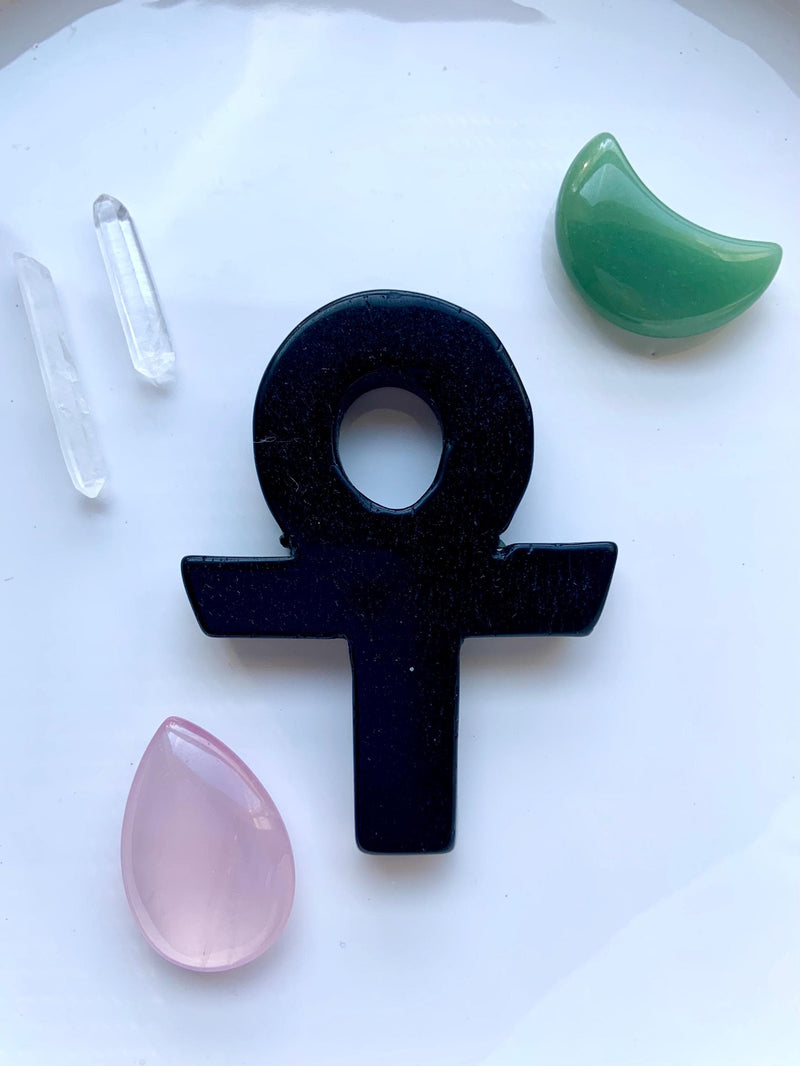 A Black Obsidian Crystal Ankh Carving, shown on a white plate with some other crystals