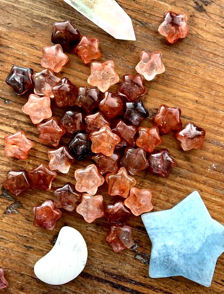 An array of vibrant red hematoid quartz mini crystal star carvings shown on a wood table 