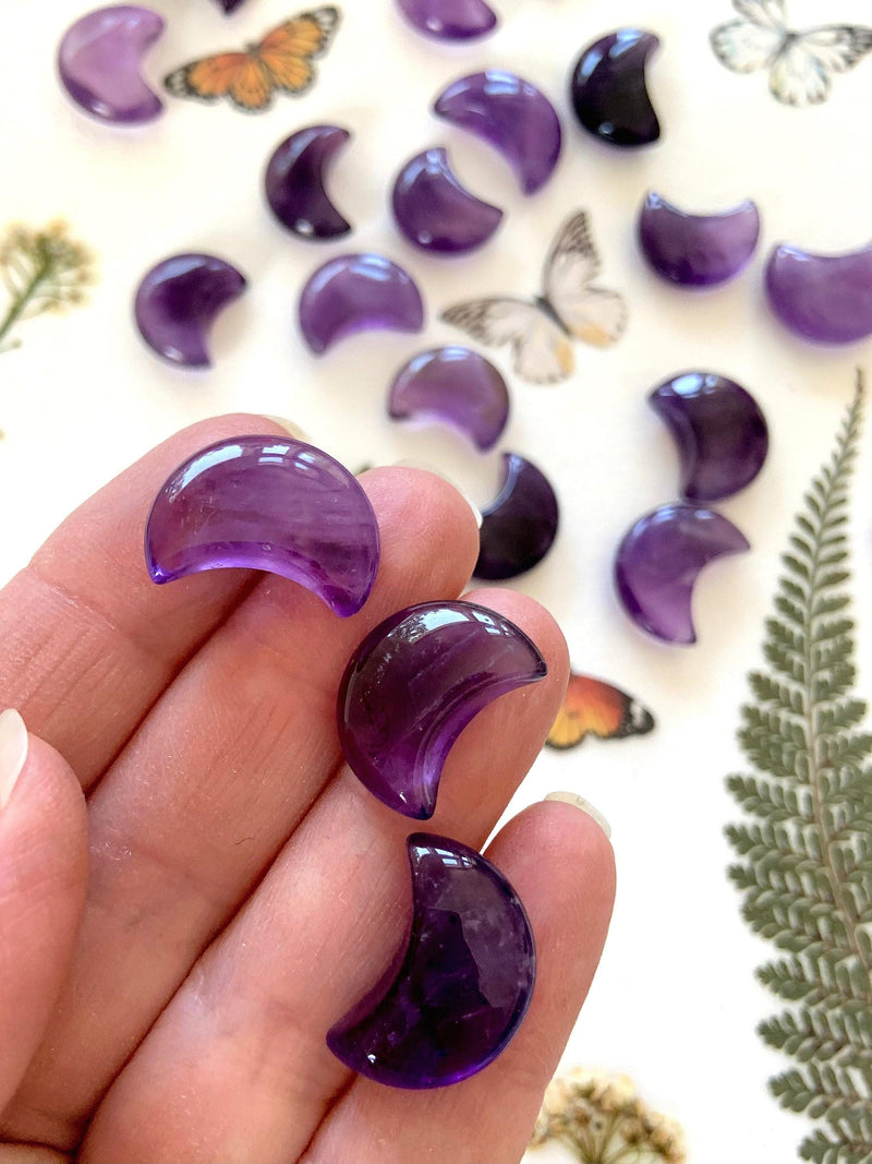 Mini sized purple amethyst moons shown on my hand with pretty crystals in the background