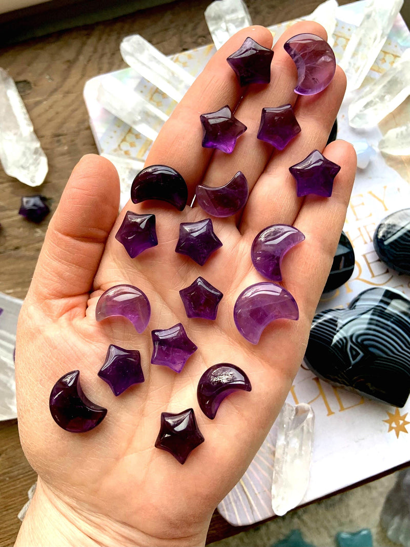 Mini sized purple amethyst moons and stars shown on my hand with pretty crystals in the background