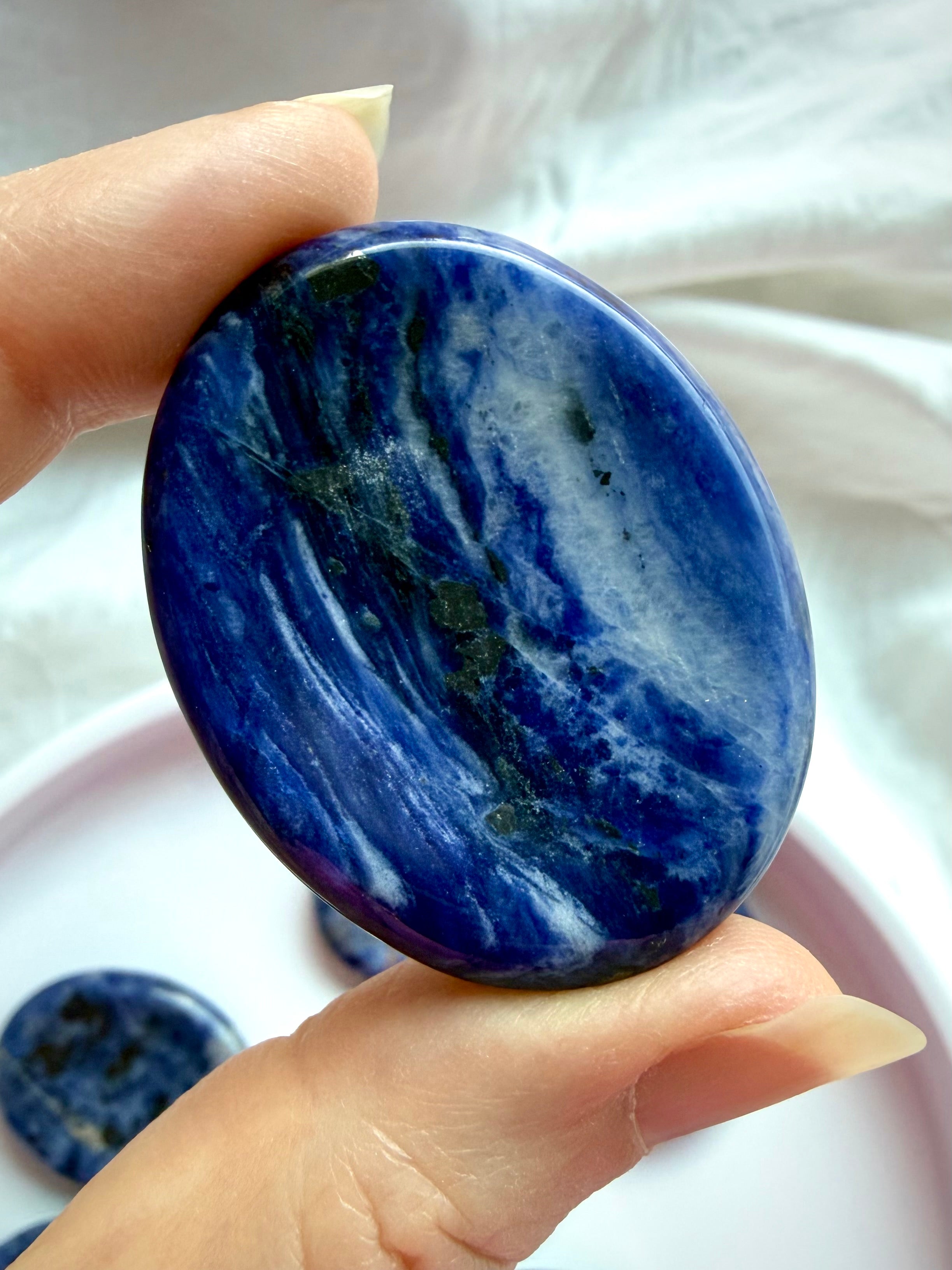 Polished Sodalite worry stone held between fingers showing deep cobalt blue color and natural white mineral veining
