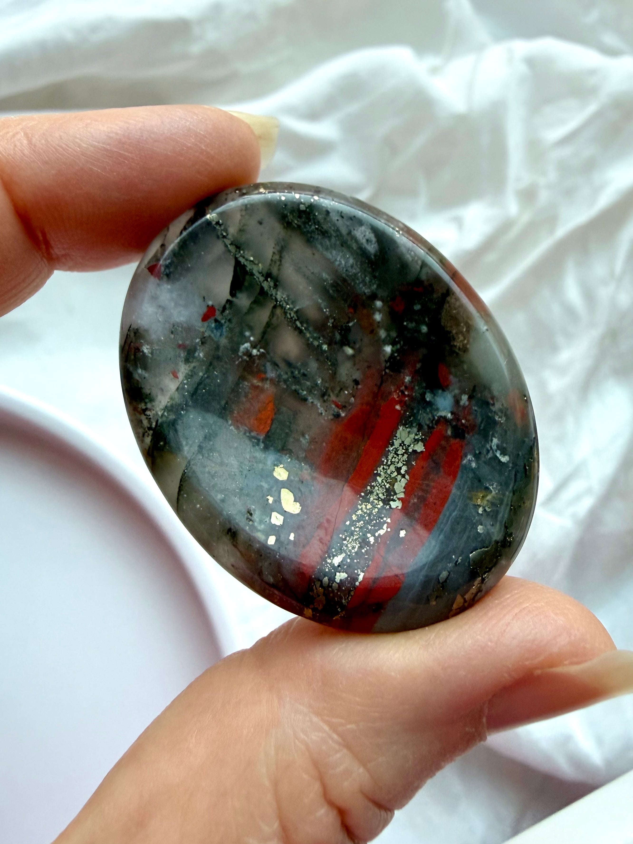 Polished Bloodstone worry stone held between fingers showing rich green tones, red inclusions, and natural mineral patterns