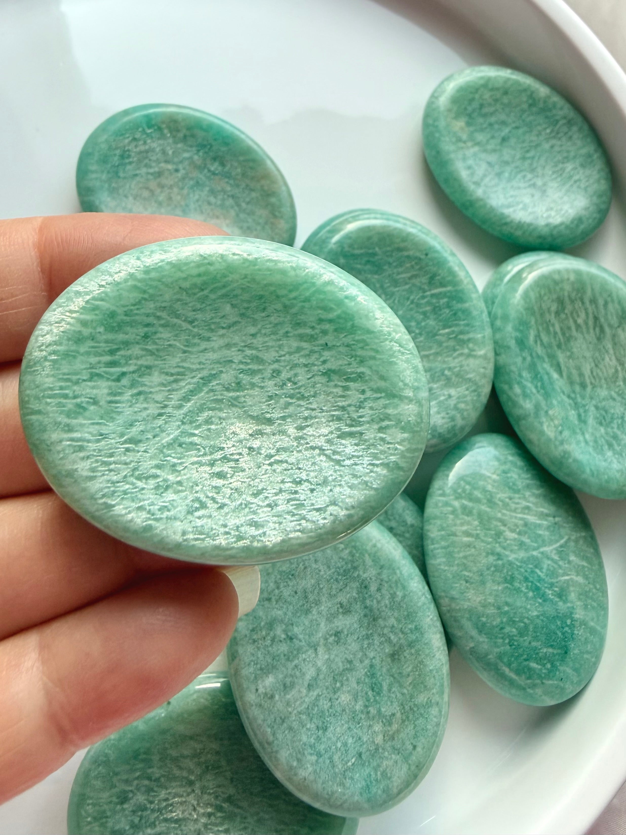 Natural Amazonite worry stone held between fingers, showing soft blue-green coloring, subtle white streaks and smooth polished surface