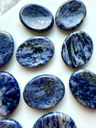 Assortment of polished Sodalite oval thumb stones with denim blue coloring and contrasting mineral inclusions