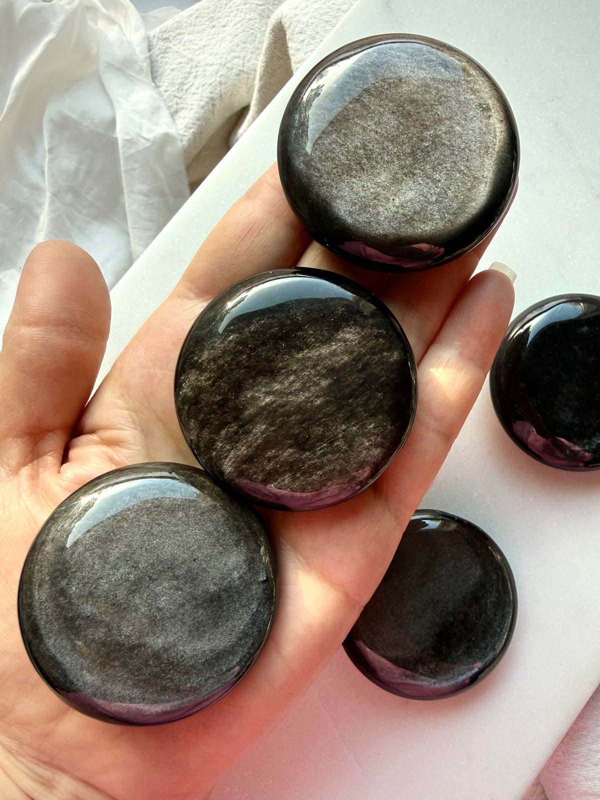 Silver Sheen Obsidian palm stones held in hand showing their round shape, polished finish, and natural variations