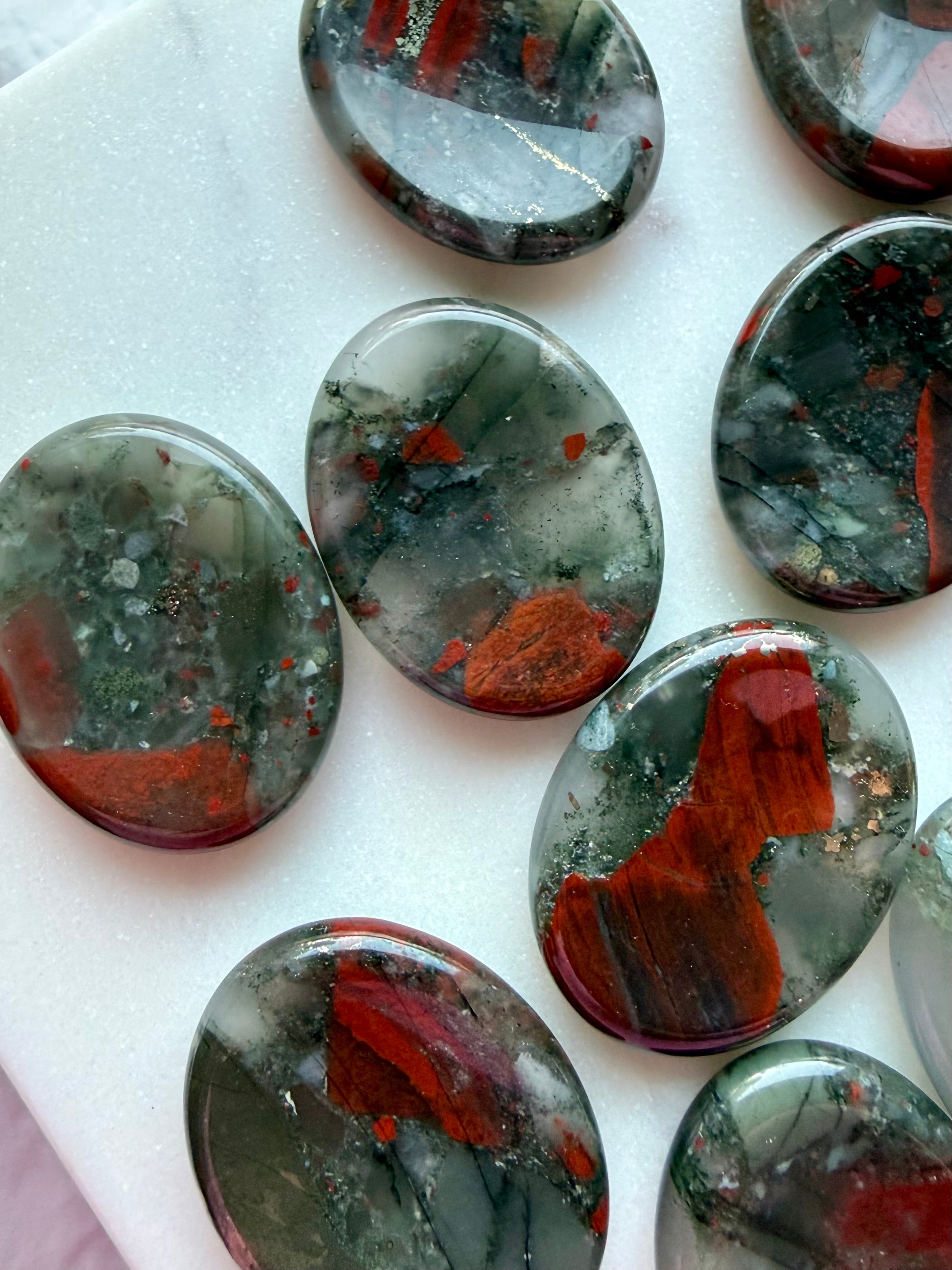 Collection of natural Bloodstone worry stones with varied red inclusions, green mineral patterns, and polished surfaces
