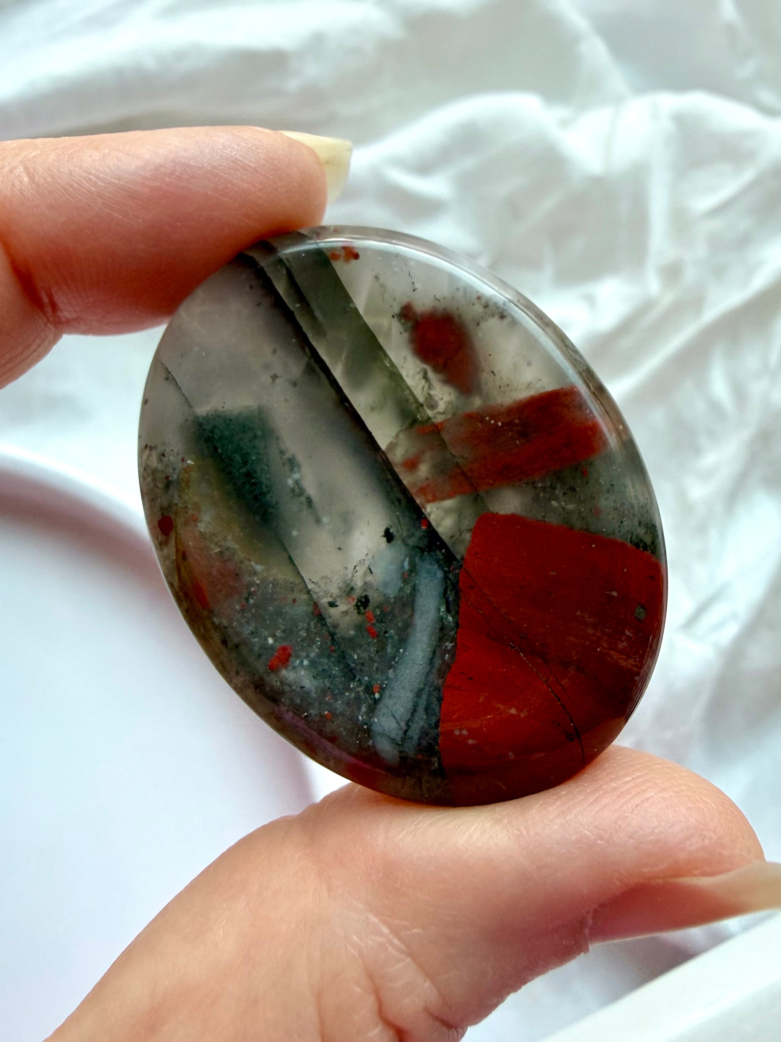 Close-up of polished Bloodstone worry stone with earthy green tones and contrasting red inclusions, pocket crystal for courage