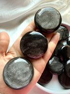 Silver Sheen Obsidian palm stone held in hand showing its round disc shape and shifting silvery sheen