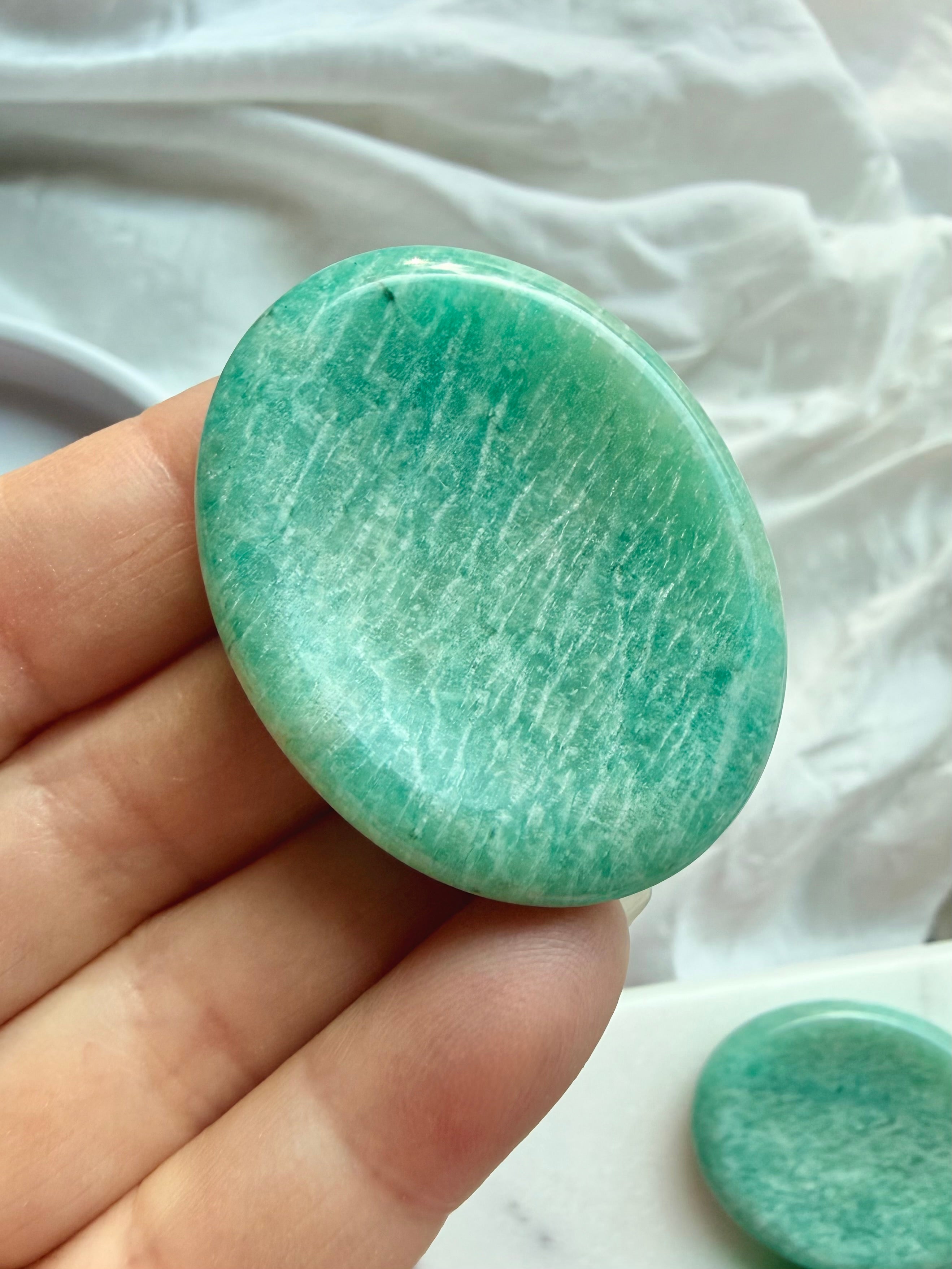 Natural Amazonite crystal worry stone held in hand, featuring beautiful seafoam-green tones and subtle white mineral inclusions