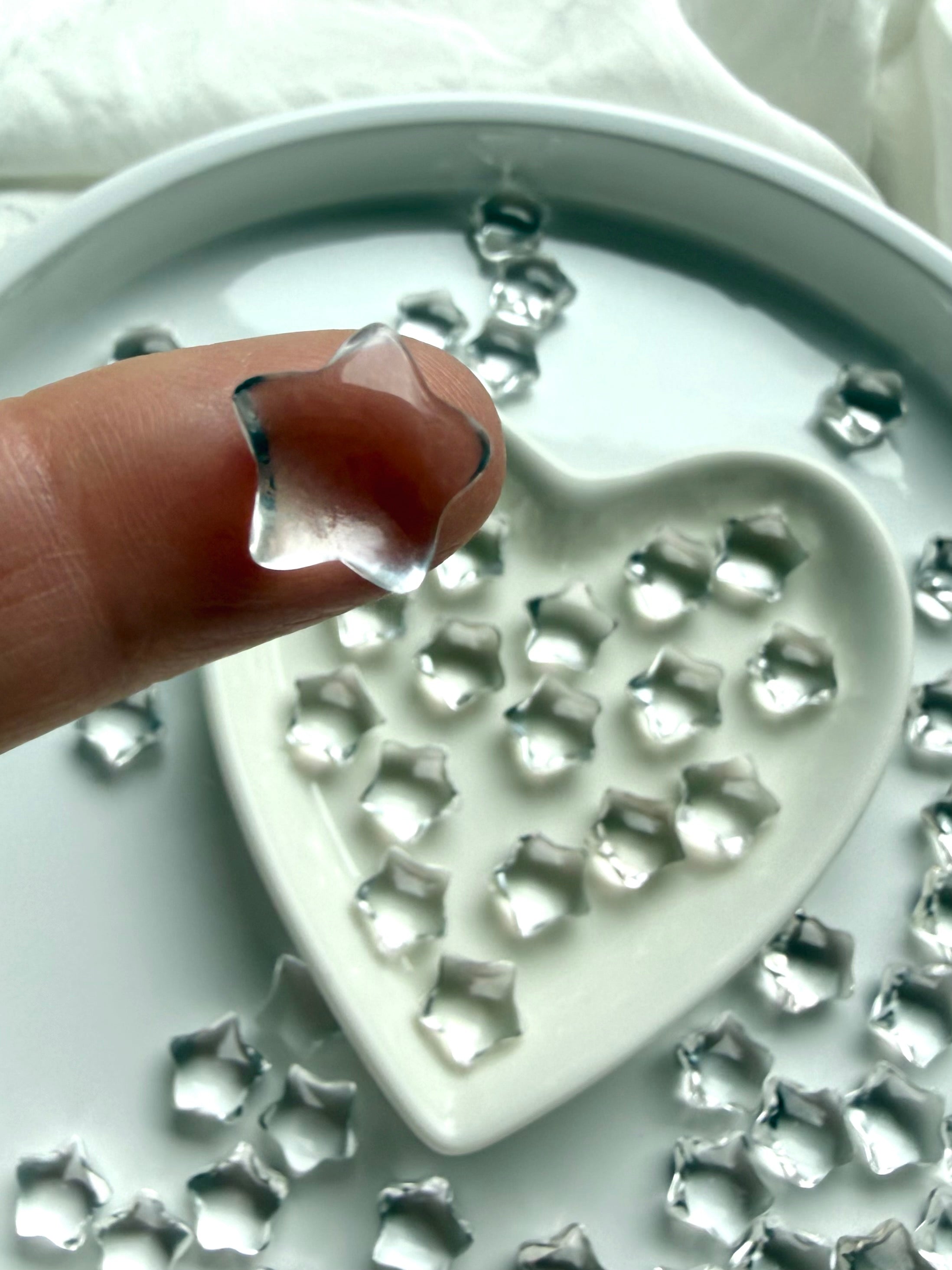 Small Clear Quartz star balanced on a fingertip above a heart-shaped dish, transparent crystal carving for intention setting and spiritual clarity