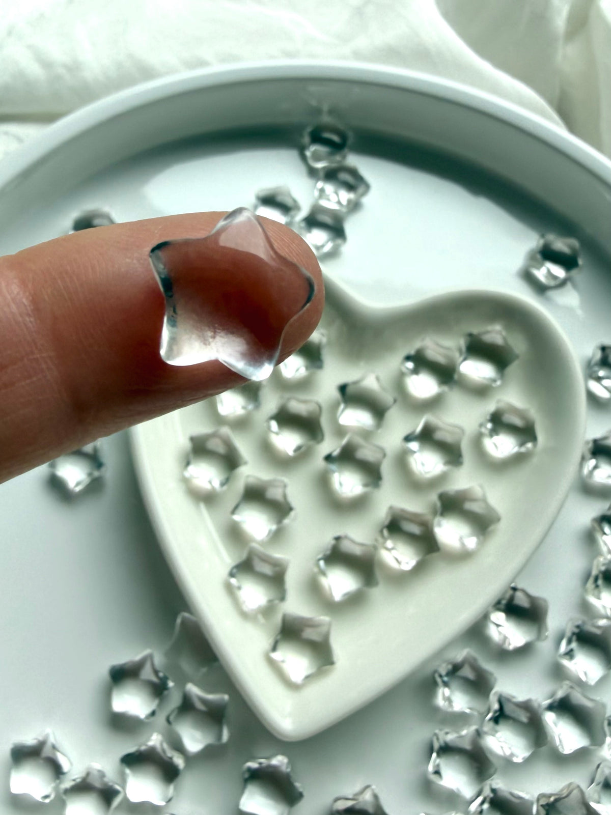 Small Clear Quartz star balanced on a fingertip above a heart-shaped dish, transparent crystal carving for intention setting and spiritual clarity