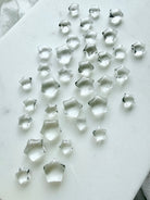 Tiny Clear Quartz star gemstones arranged on a white background, polished five-point crystal stars for crafting, meditation and energy healing