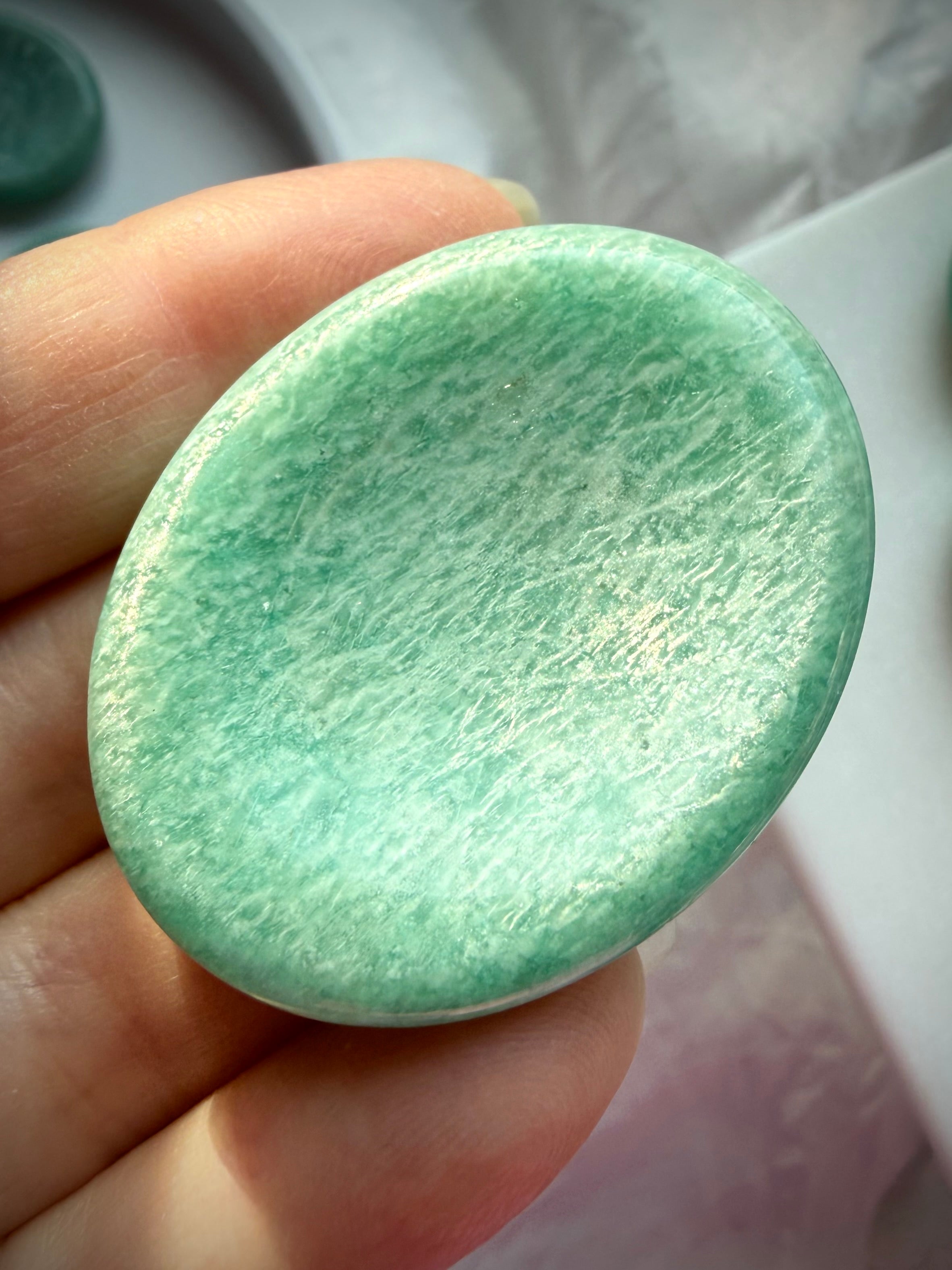 Amazonite thumb stone held between fingers, highlighting its glossy polish, natural white veining and soothing turquoise-green color