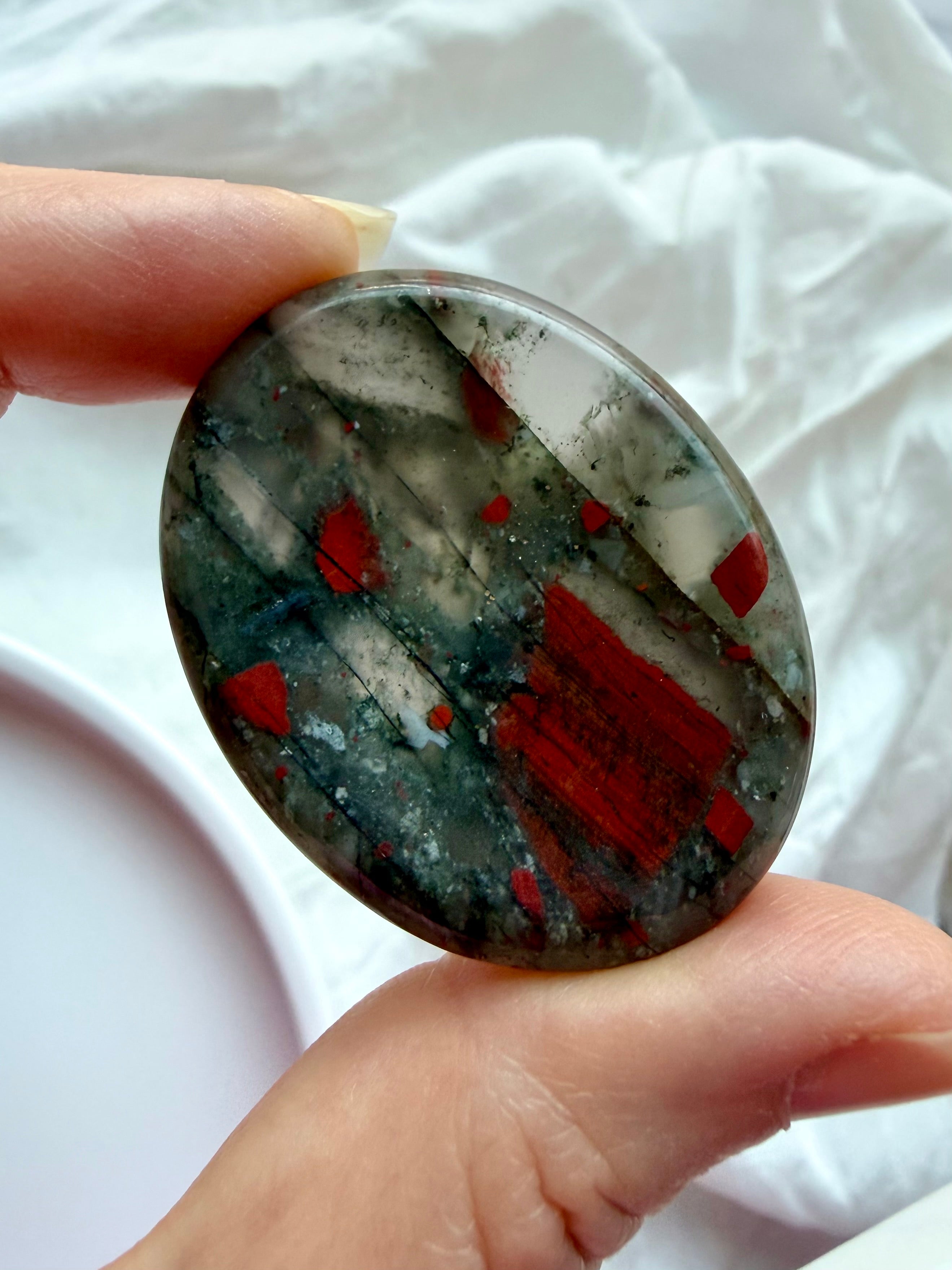 Polished Bloodstone worry stone held between fingers showing natural mineral inclusions and smooth surface for stress relief