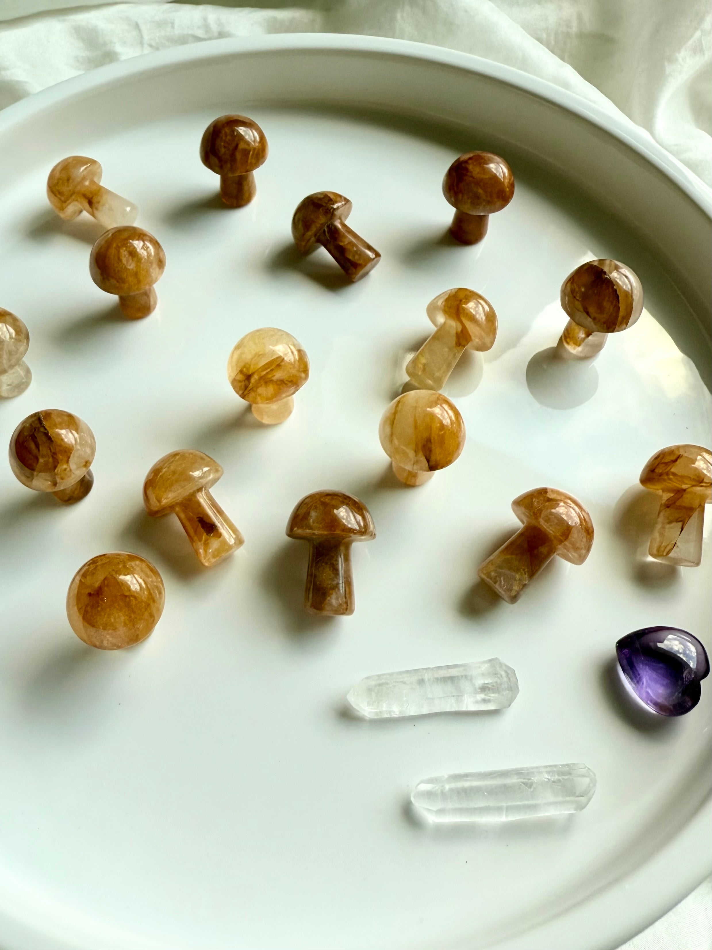 Golden Healer Quartz crystal mushrooms displayed on white tray with clear quartz points and amethyst heart — mini carvings for Solar Plexus healing.