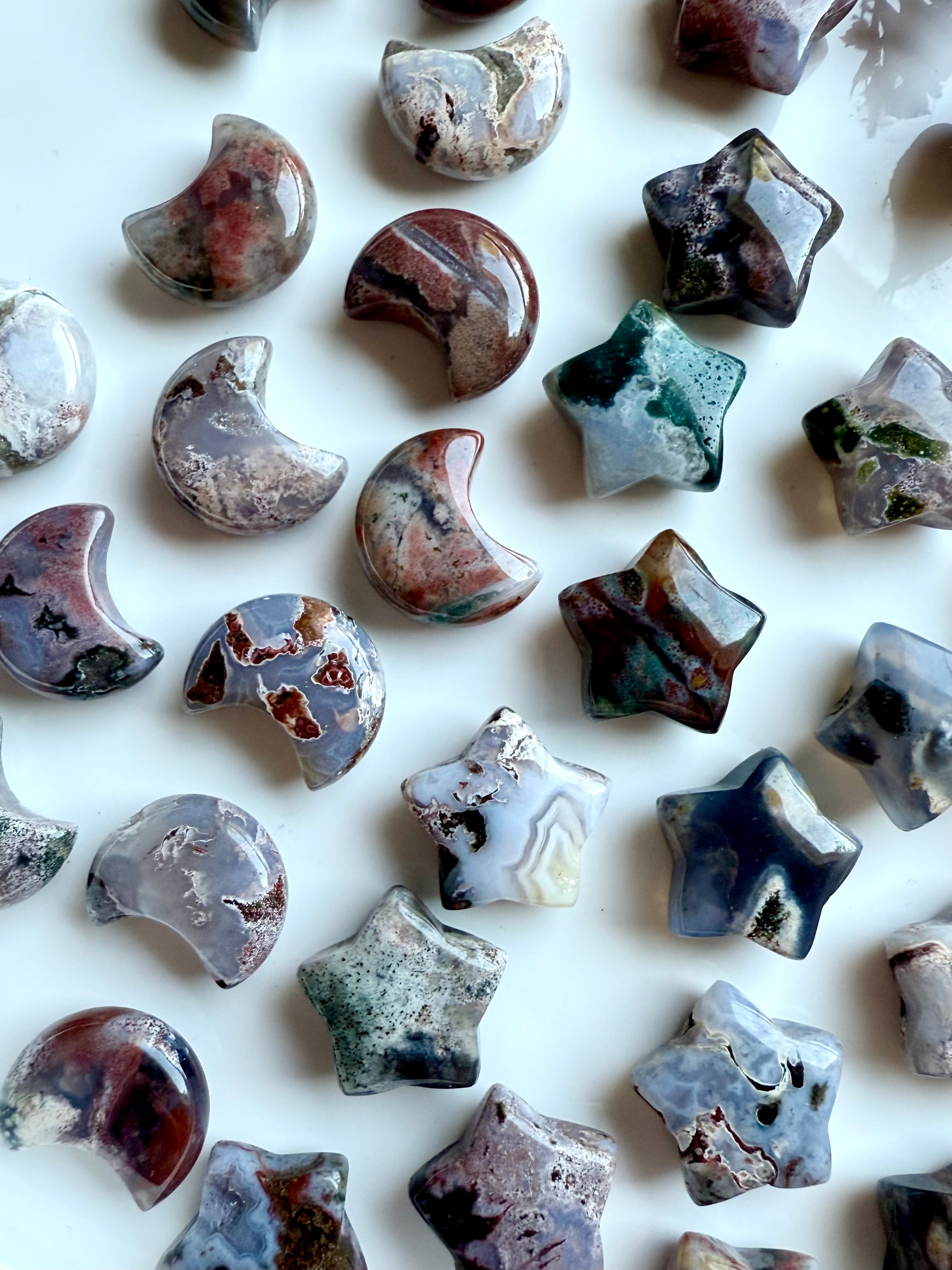 Assortment of Ocean Jasper moons and stars on a white tray — mini gemstone carvings in unique cosmic patterns for altar and crystal grids