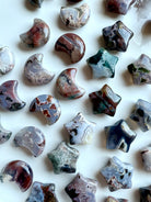 Assortment of Ocean Jasper moons and stars on a white tray — mini gemstone carvings in unique cosmic patterns for altar and crystal grids