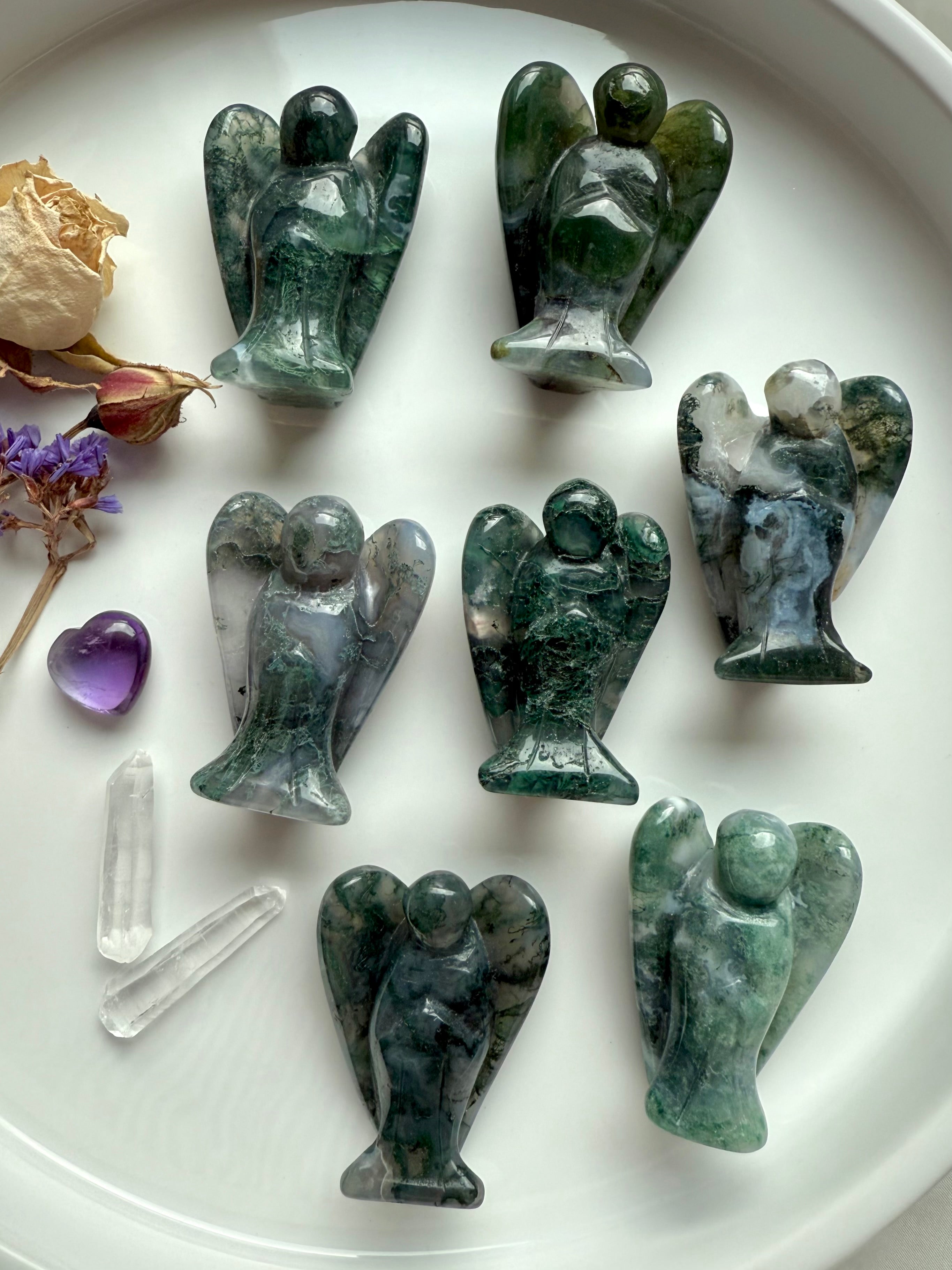 Moss Agate crystal angel figurines — group display on white plate showing natural variations, grounding energy, and heart-centered healing.