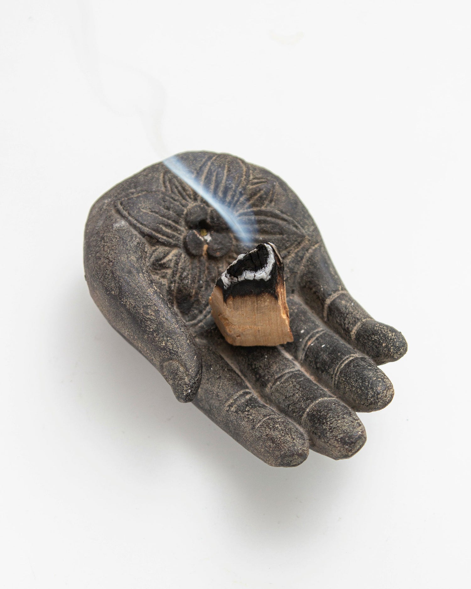 Palo Santo stick burning on ceramic Buddha hand holder – smudge ritual setup for purification and mindful practice