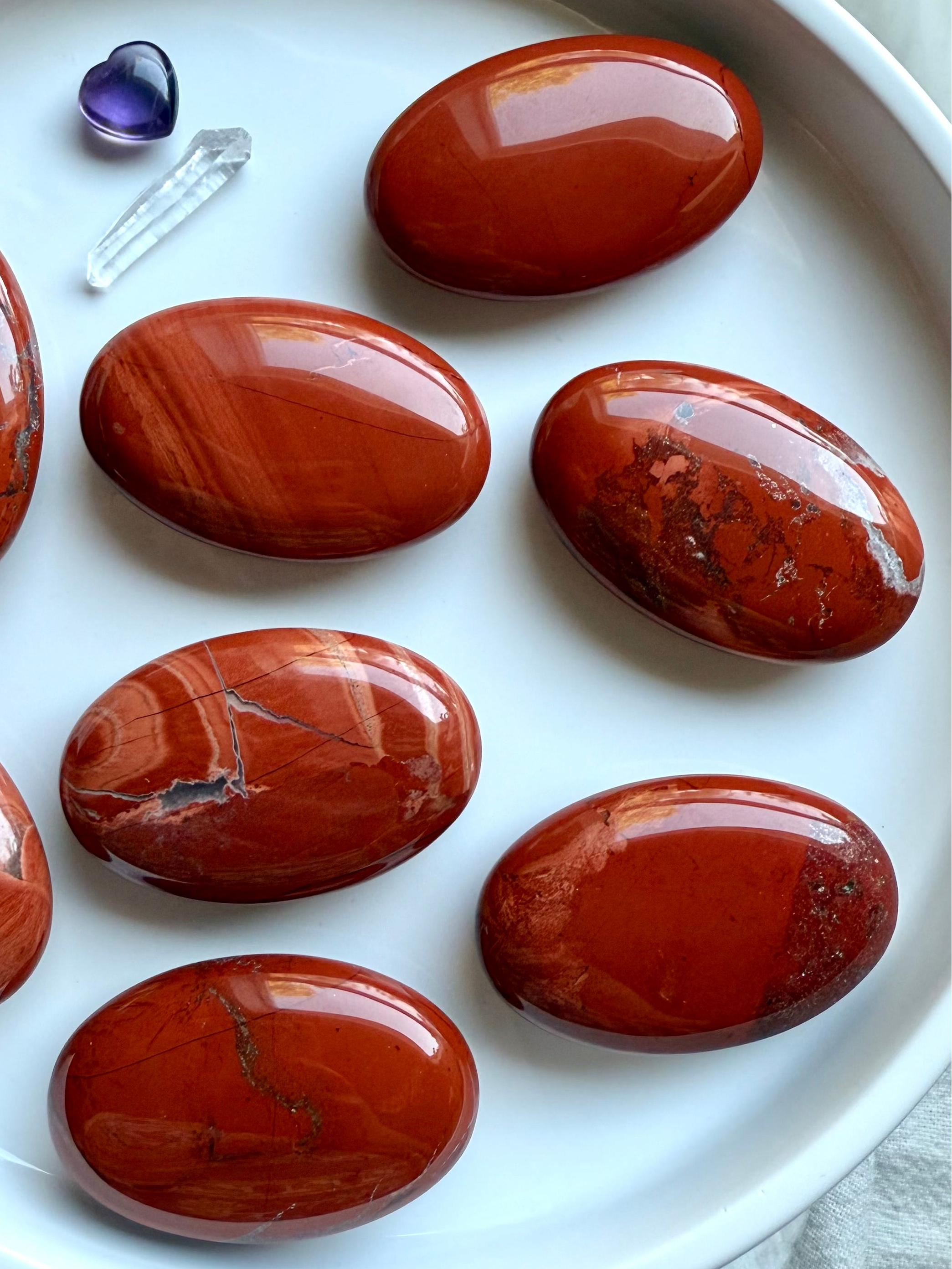Brilliant Red Jasper palm stones on a white plate — grounding Root Chakra crystals for meditation, showing natural color and pattern variation.