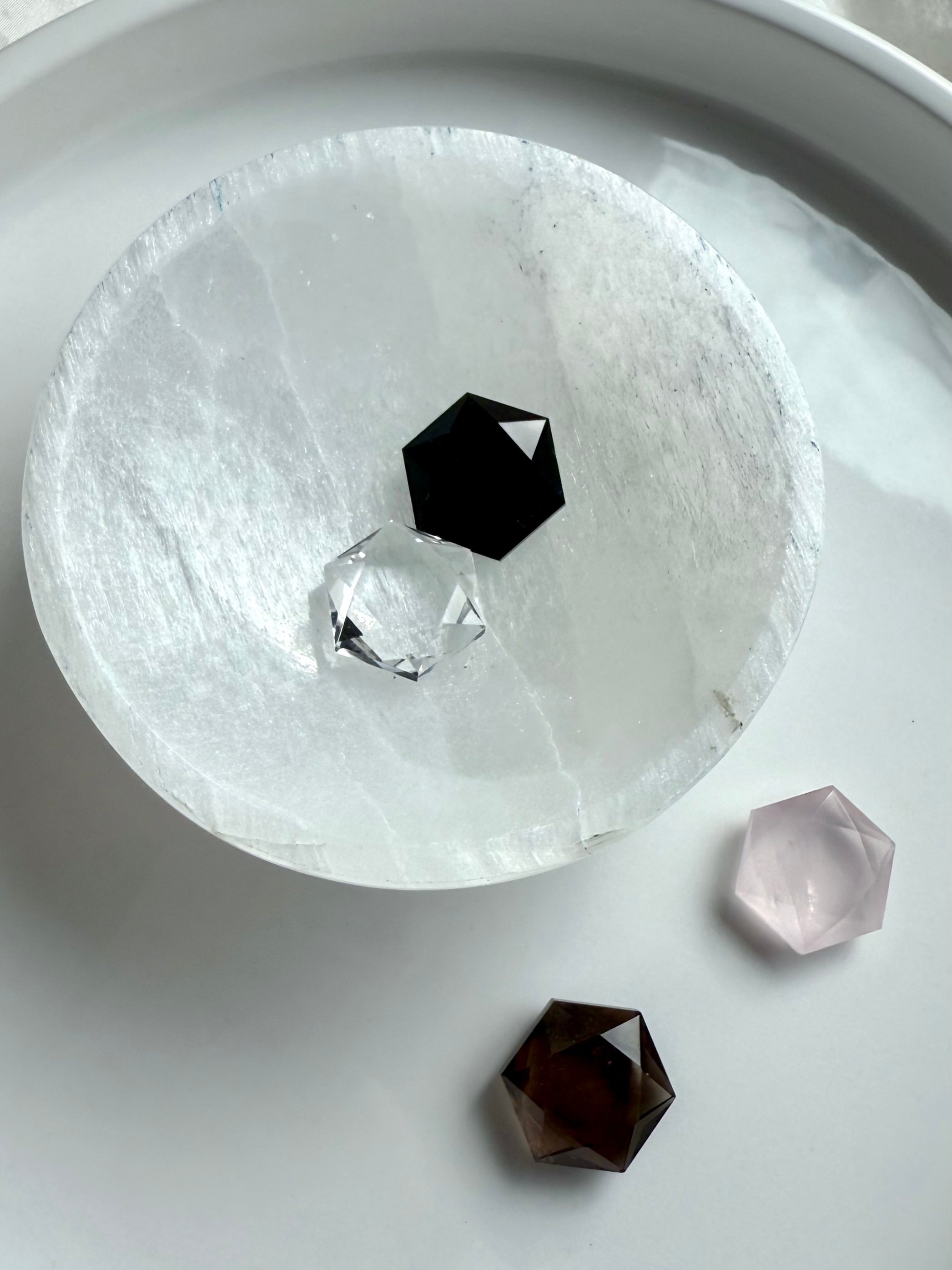 Round selenite charging plate showcasing faceted crystal hexagons in black obsidian, clear quartz, rose quartz, and smoky quartz