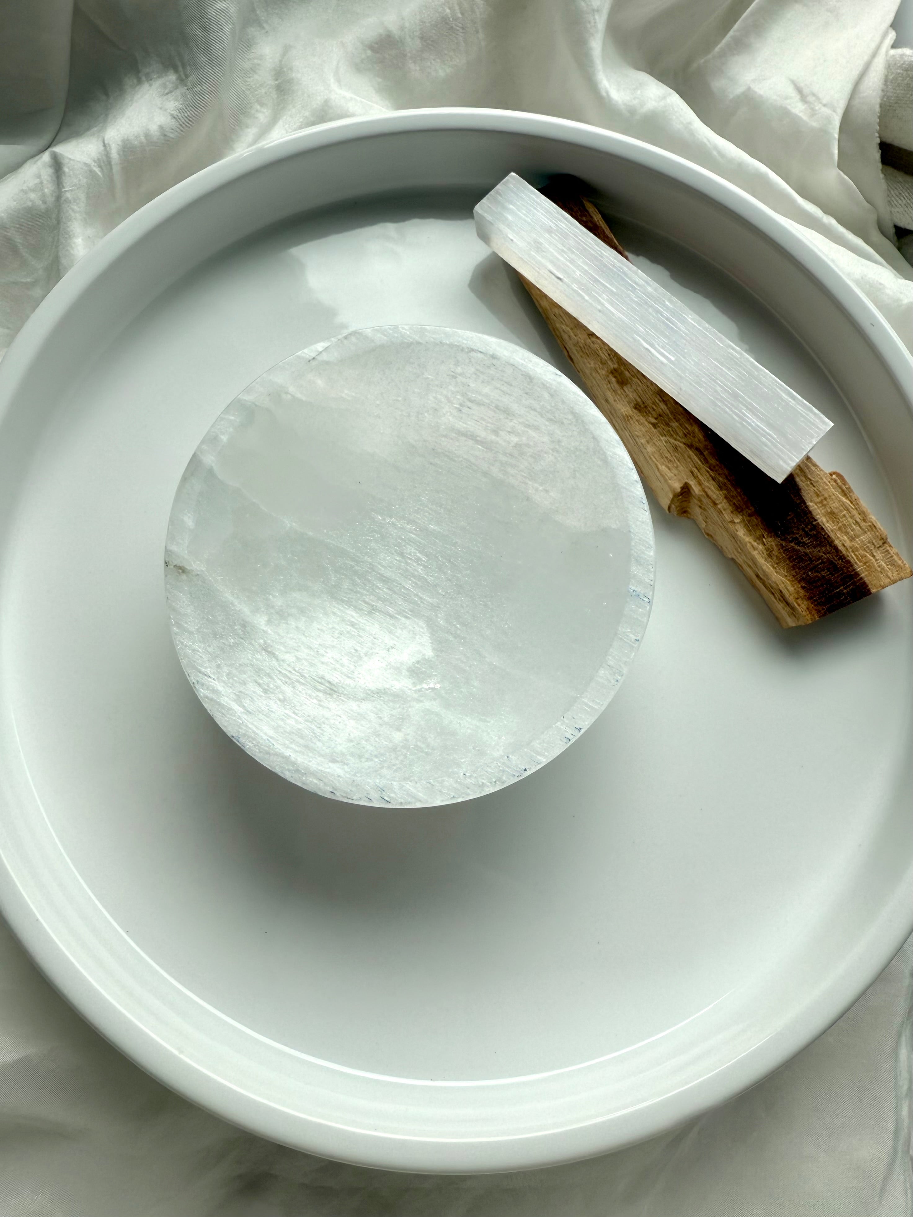 Round selenite charging bowl styled with Palo Santo and selenite wand for energy clearing rituals