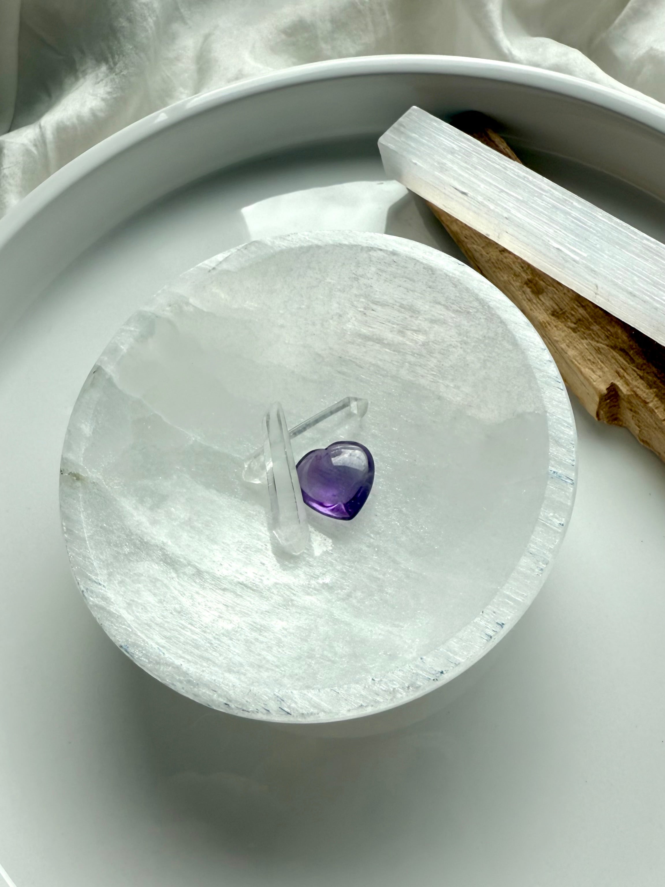 Mini amethyst heart and clear quartz wand displayed on round selenite bowl for chakra cleansing