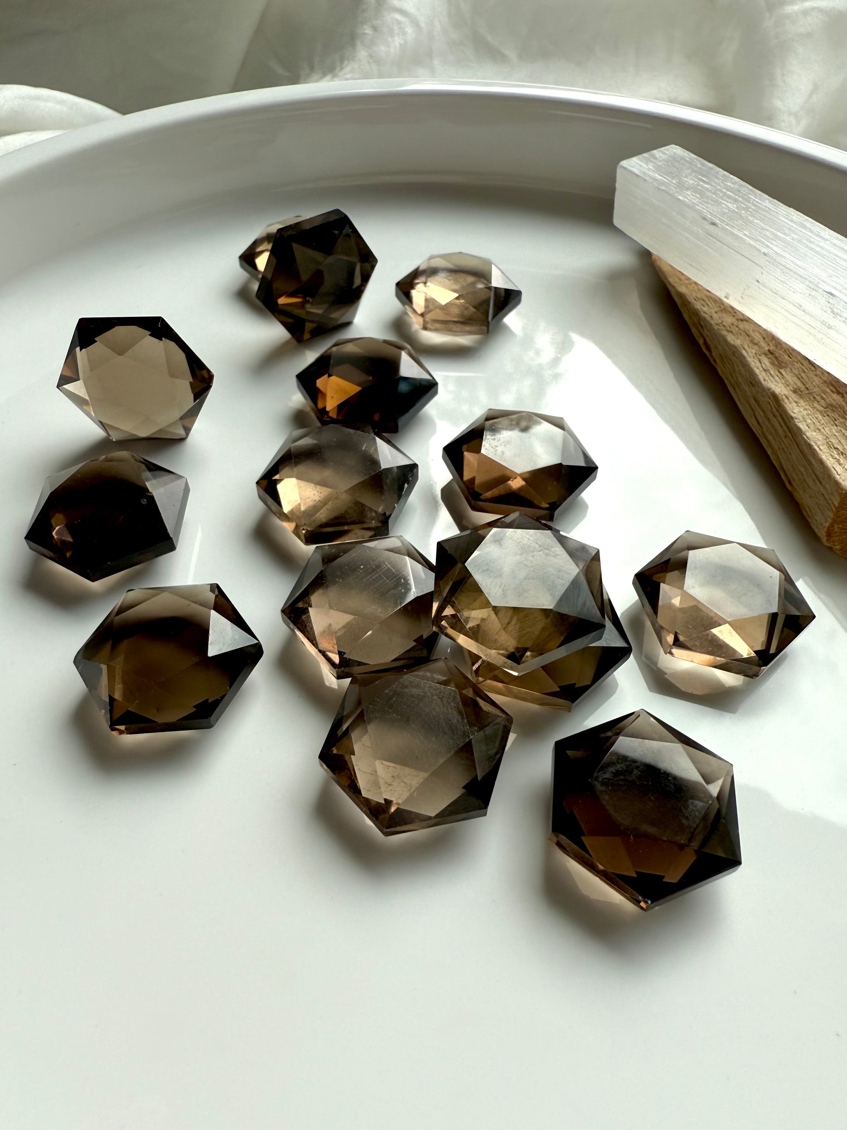 Faceted smoky quartz hexagon crystals arranged in a white dish with selenite and palo santo – grounding Root Chakra stones for energy clearing and healing.