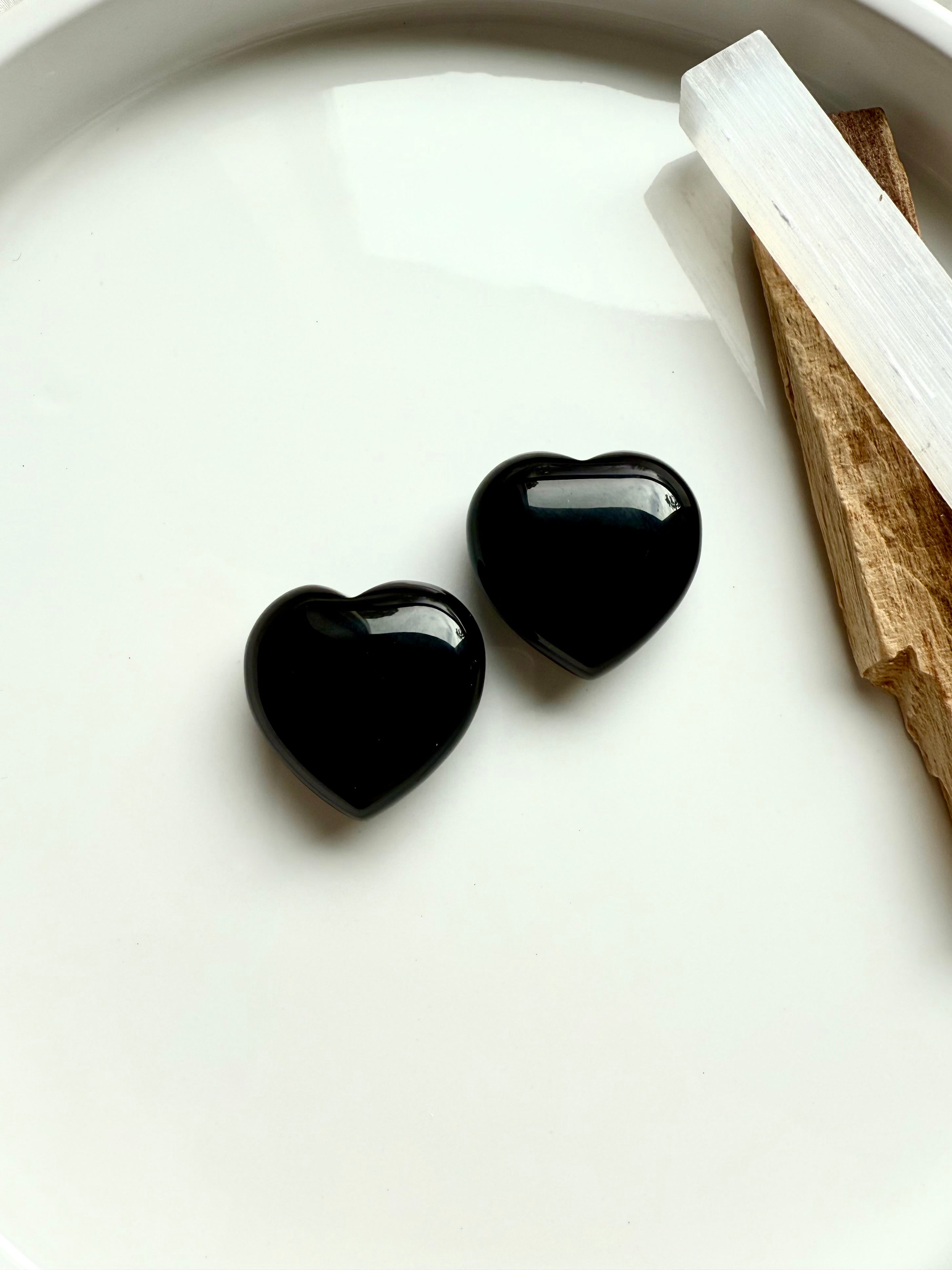 Two polished Black Obsidian hearts with selenite and palo santo — crystals for energetic protection, clearing, and Root Chakra grounding.