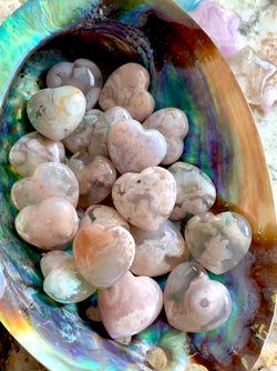 A colorful array of mini flower agate heart shapes inside an abalone shell