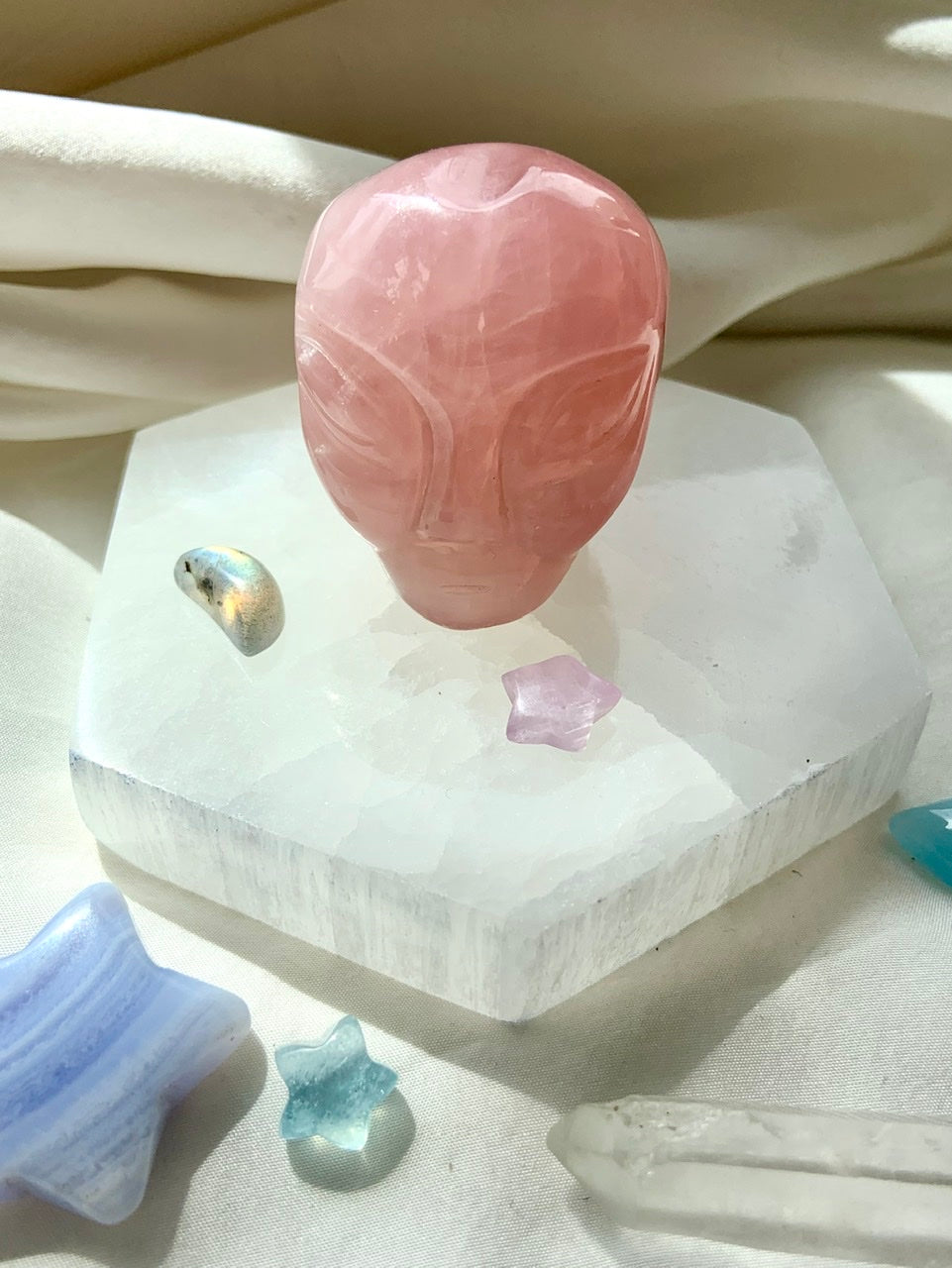 Rose Quartz alien head carving displayed on hexagon selenite plate with crystal stars – heart chakra healing crystal for cosmic love