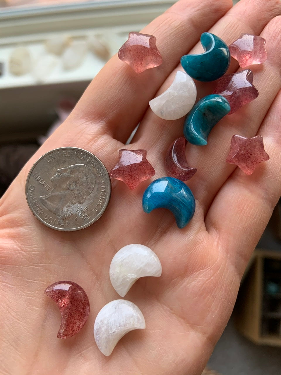 Mini Strawberry Quartz moons and stars shown with blue apatite and moonstone carvings — size comparison with quarter on hand