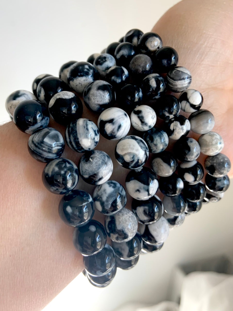 Side view of multiple Orca Agate bracelets stacked on wrist, showing bold black-and-white banded patterns with subtle gray marbling in polished round beads
